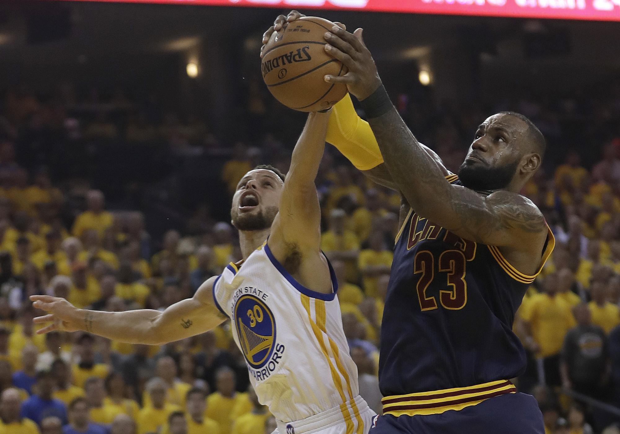 El alero de Cleveland Cavaliers LeBron James (23) atrapa un rebote contra el guardia de Golden State Warriors Stephen Curry (30). 