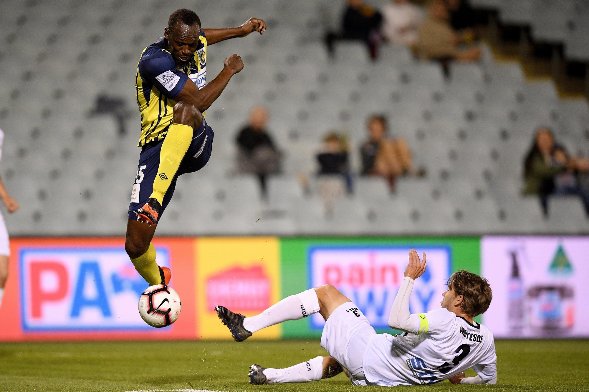 El jugador de los Marineros y la atleta jamaicano Usain Bolt (i) recibe una entrada de Tom Whiteside durante el partido de la Liga Australiana de fútbol que enfrentó a los Marineros y el Macarthur Sur West United, en el estadio Campbelltown de Sídney (Australia), el 12 de octubre de 2018. 