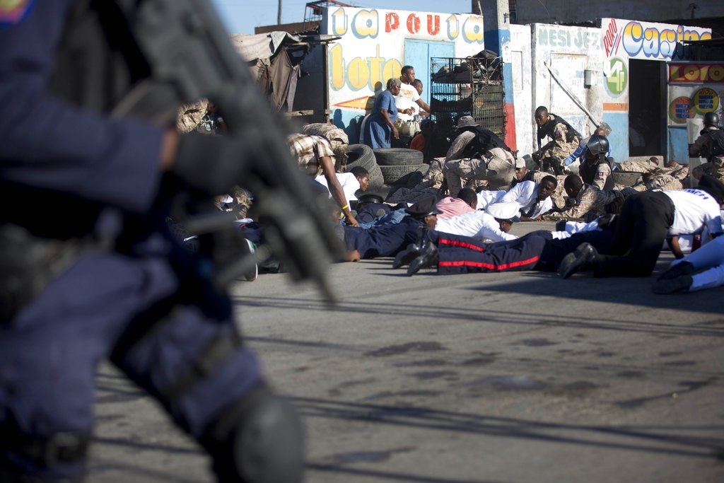 La policía haitiano se cubre durante un tiroteo al final de una ceremonia que conmemoraba el 212 aniversario del asesinato del héroe de la independencia, el general Jean-Jacques Dessalines, en Puerto Príncipe, Haití. 