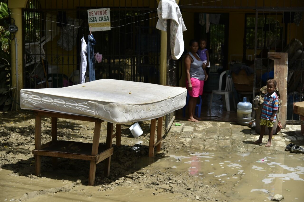 Una mujer y dos niños observan el colchón fuera de la vivienda , la cual está en medio de un lodazal, en el sector El Tamarindo, en La Vega.