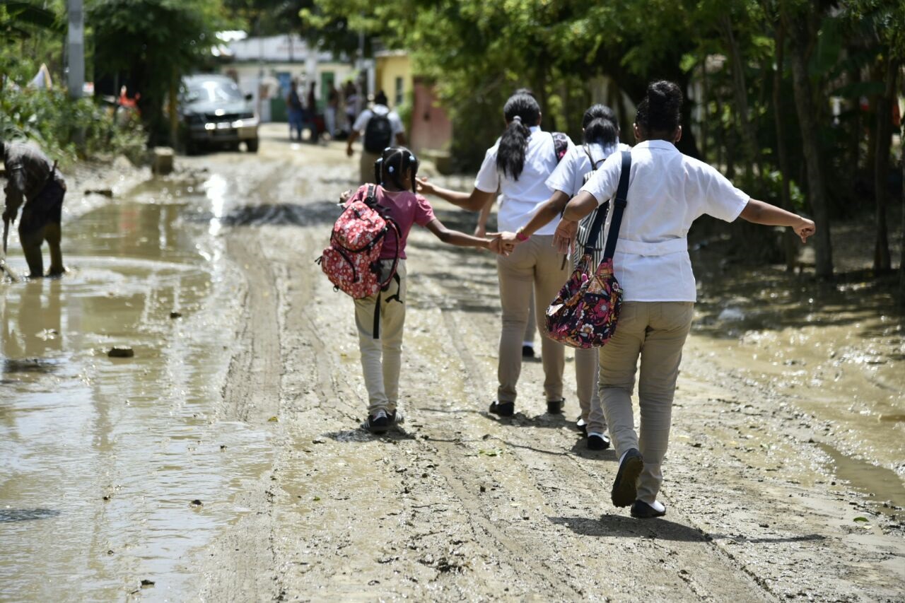 Niños se dirigen a la escuela tratando de evadir el lodo de una calle del sector El Tamarindo, en La Vega.
