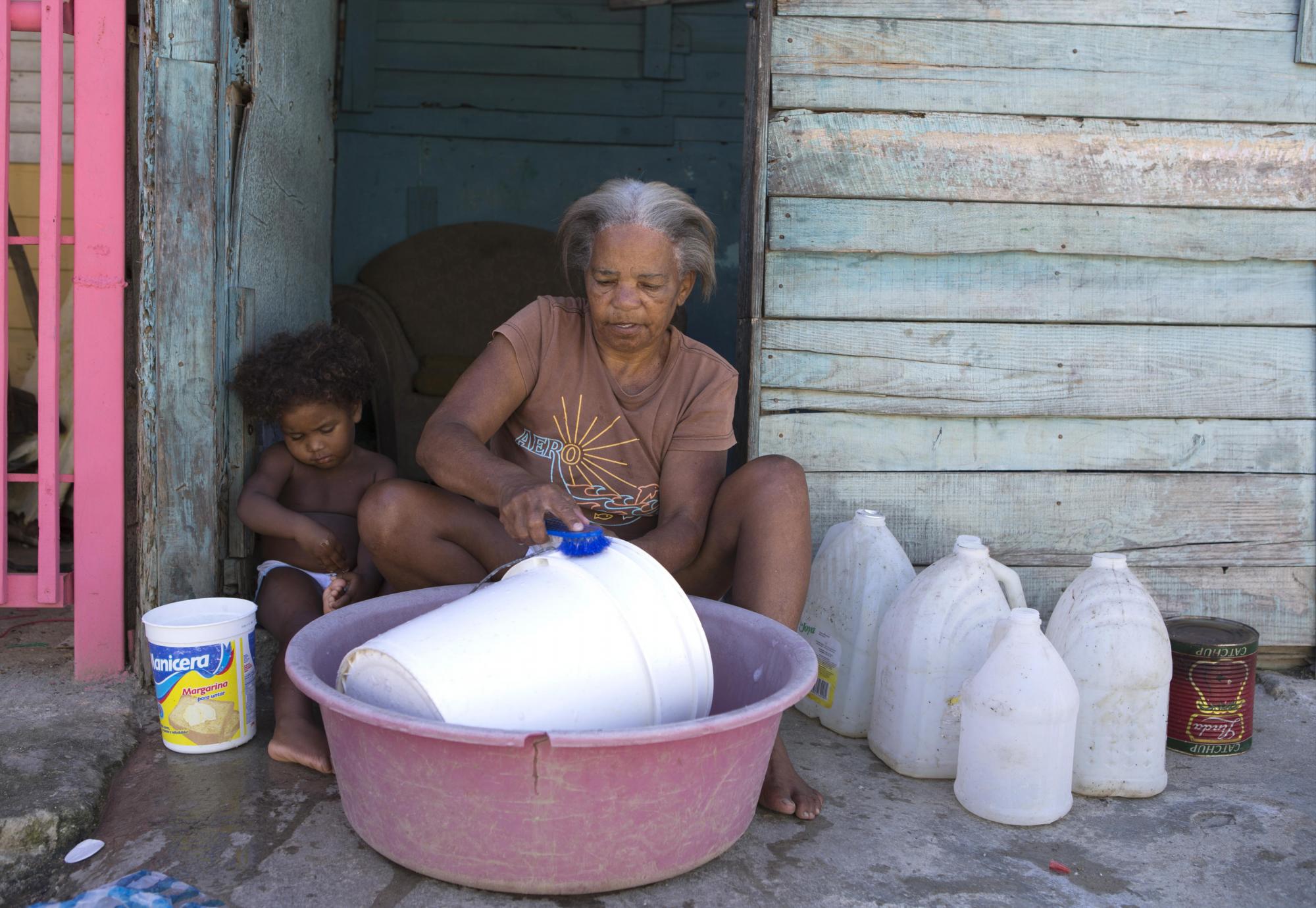 Fotografía fechada el 11 de octubre de 2017 que muestra a Irene de los Santos, de cincuenta y seis años, mientras lava bidones para acumular agua en su casa en el albergue de Canta La Rana, en el municipio dominicano de Los Alcarrizos, en Santo Domingo (República Dominicana). 