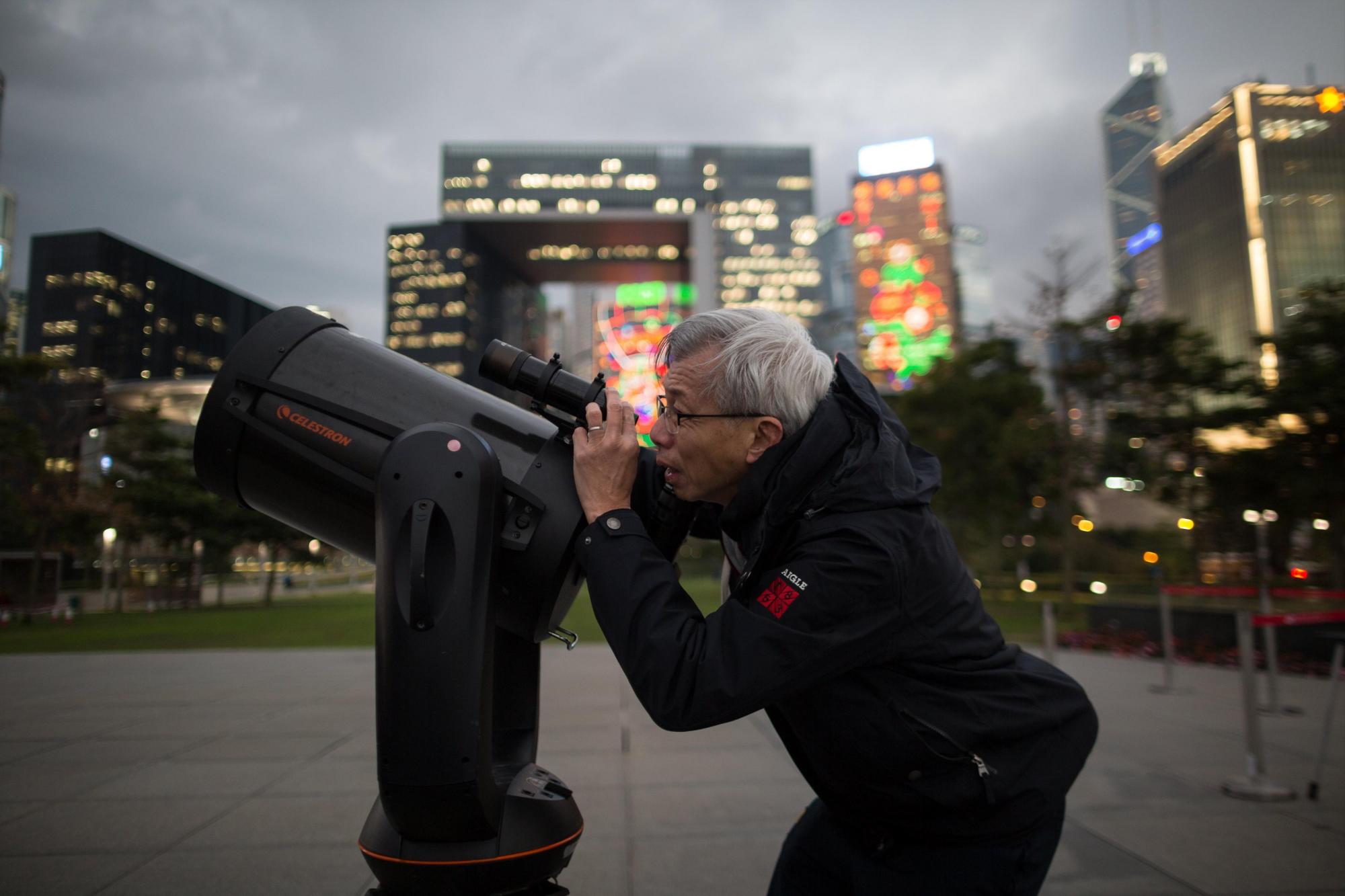 Un hombre ajusta un telescopio mientras espera a que la llamada superluna azul sea visible en Hong Kong, China, hoy, 31 de enero de 2018. 