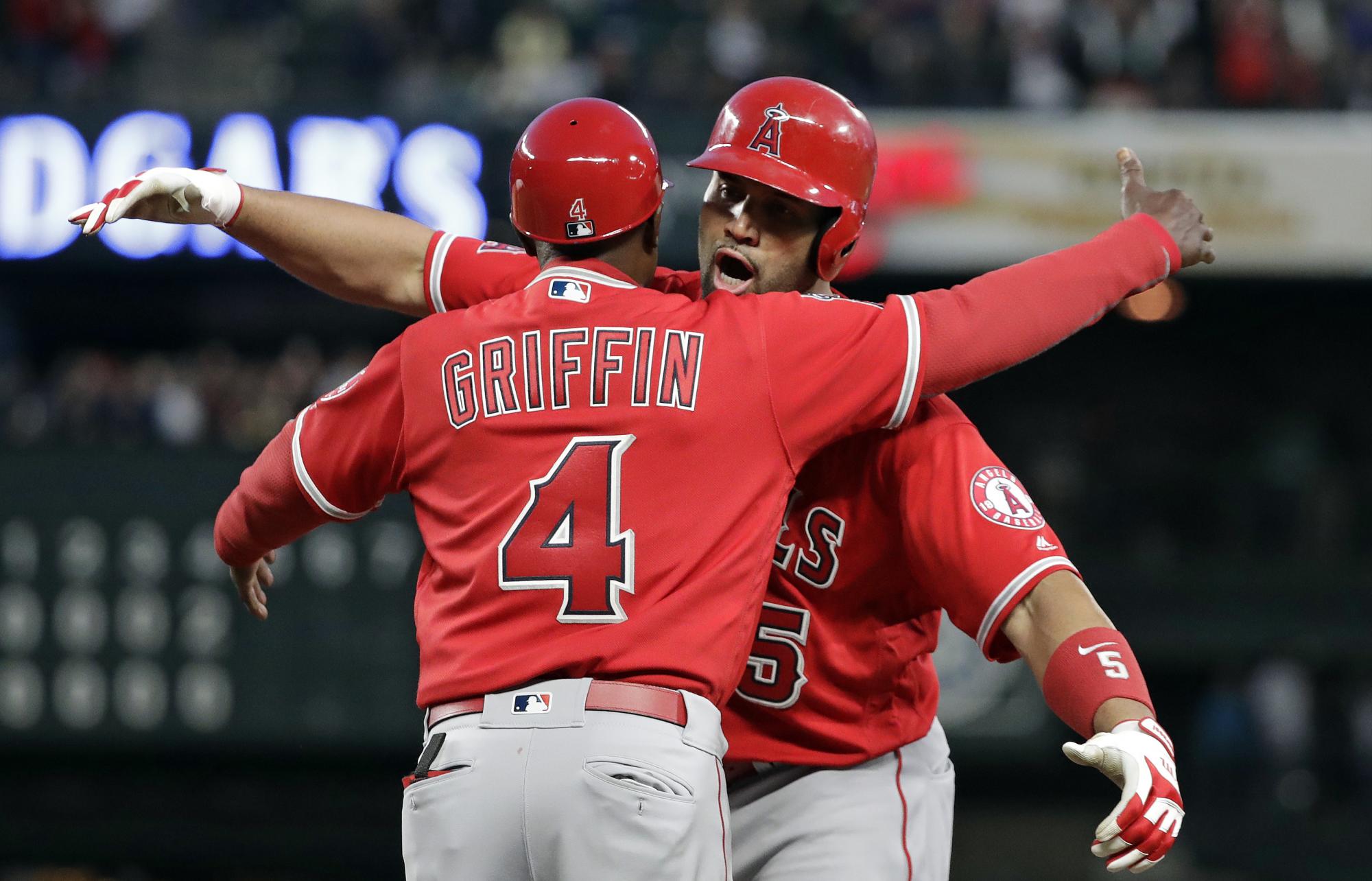 Albert Pujols de los Angelinos de Los Ángeles, derecha es abrazado por el coach de primera, su compatriota Alfredo Griffin luego de conectar su hit 3 mil en las Grandes Ligas, un sencillo contra los Marineros de Seattle en la quinta entrada de un partido de béisbol el viernes 4 de mayo de 2018 en Seattle.