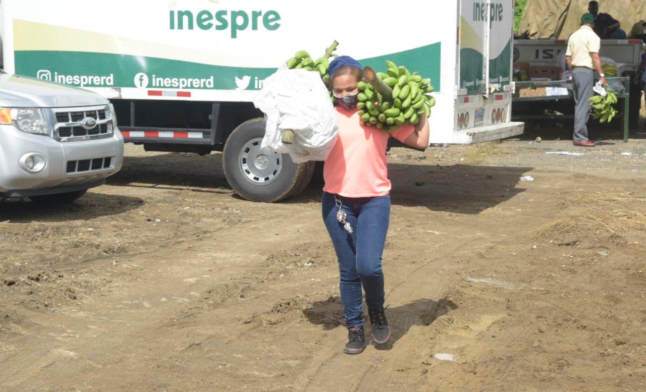Una mujer carga con dos racimo de guineos en la feria de Inespre que se inauguró hoy martes 14 de diciembre de 2021 en el solar del antiguo aeropuerto de Herrera, en Santo Domingo Oeste.