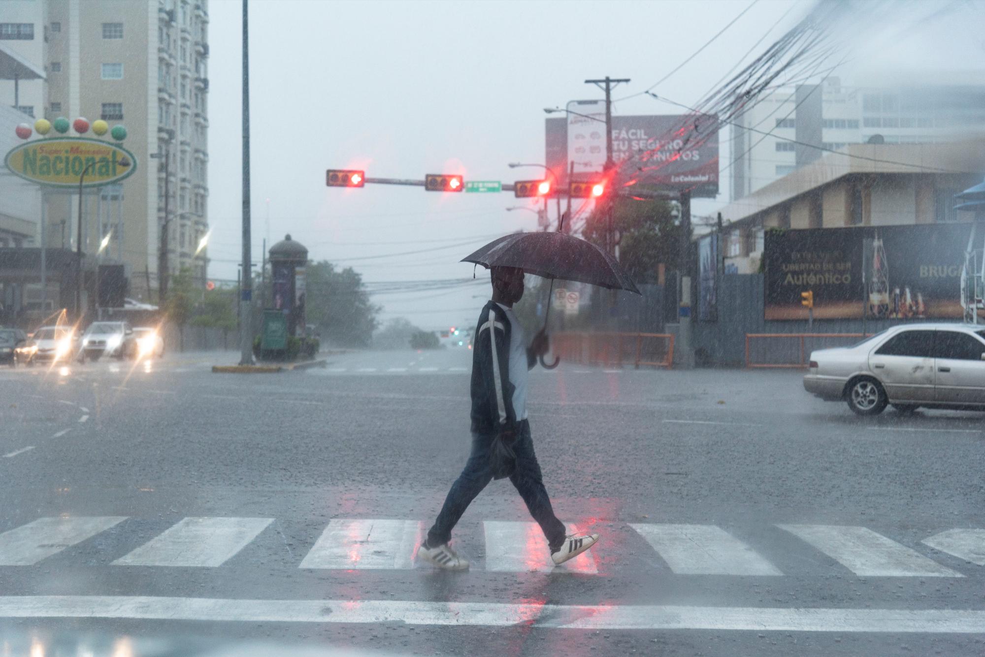 Un hombre con una sombrilla camina por el paso cebra de la intersección Abraham Lincoln con 27 de febrero por las fuertes lluvias y vientos causados por la tormenta Laura en el territorio dominicano
