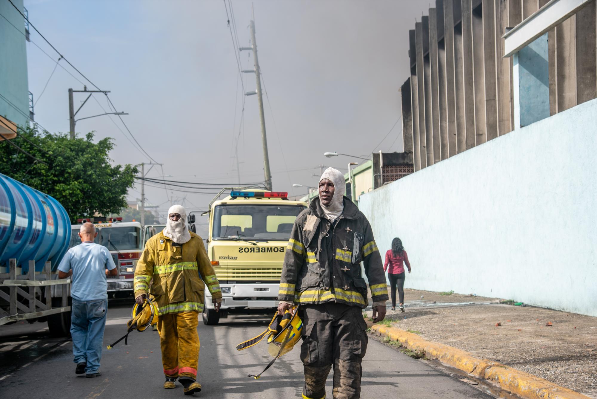 Dos miembros del Cuerpo de Bomberos del Distrito Nacional se toman un descanso luego de combatir las llamas que consumieron parte de las instalaciones de la fábrica de colchones La Reina (Foto: Juan Miguel Peña)