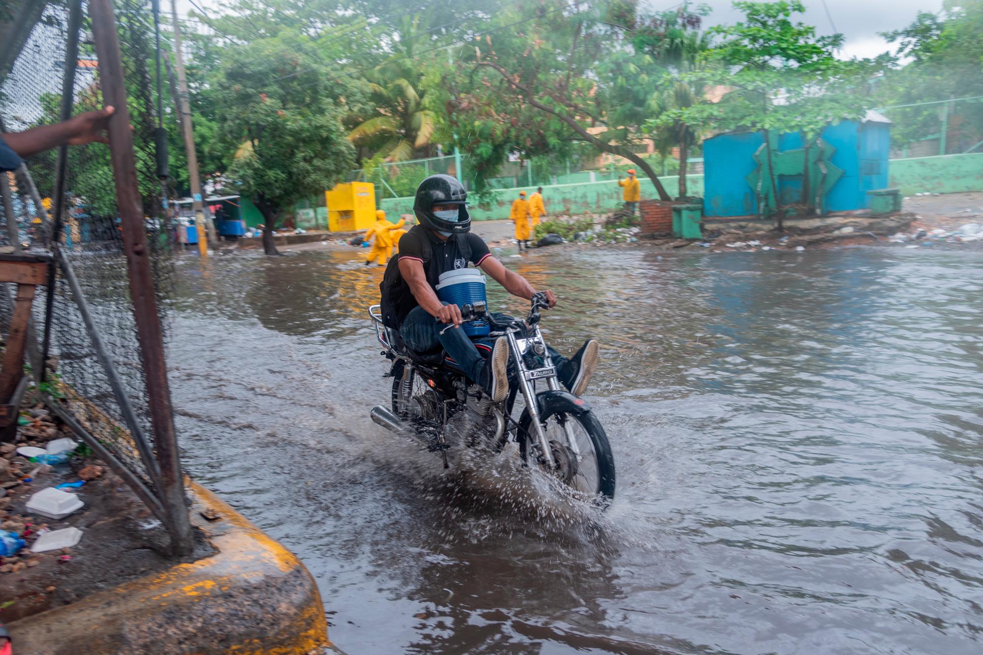 Un motorista avanza el viernes 30 de julio de 2020 por una calle de Santo Domingo inundada por las lluvias del huracán Isaías.