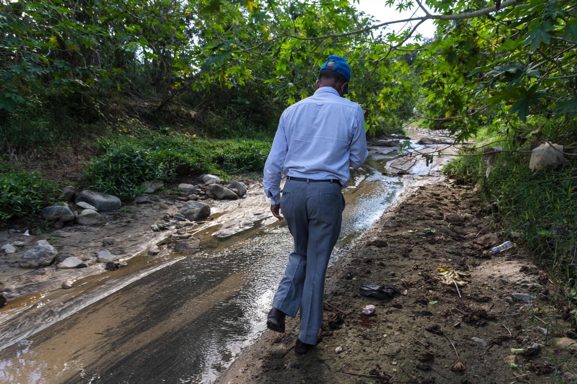El agricultor Leo Quezada camina con cuidado entre las heces fecales a orillas del afluente.