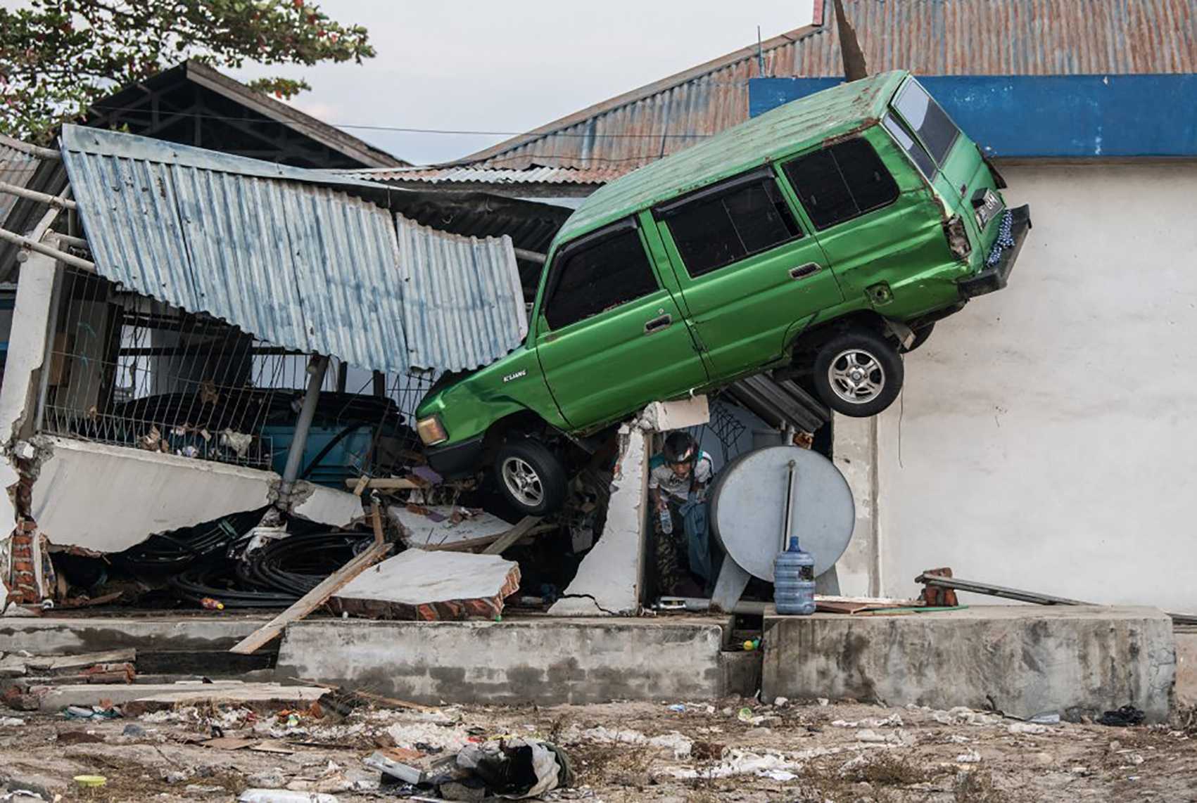 Un hombre se encuentra debajo de un automóvil que ha sido arrastrado hasta un edificio, en Palu el viernes 28 de septiembre de 2018.
