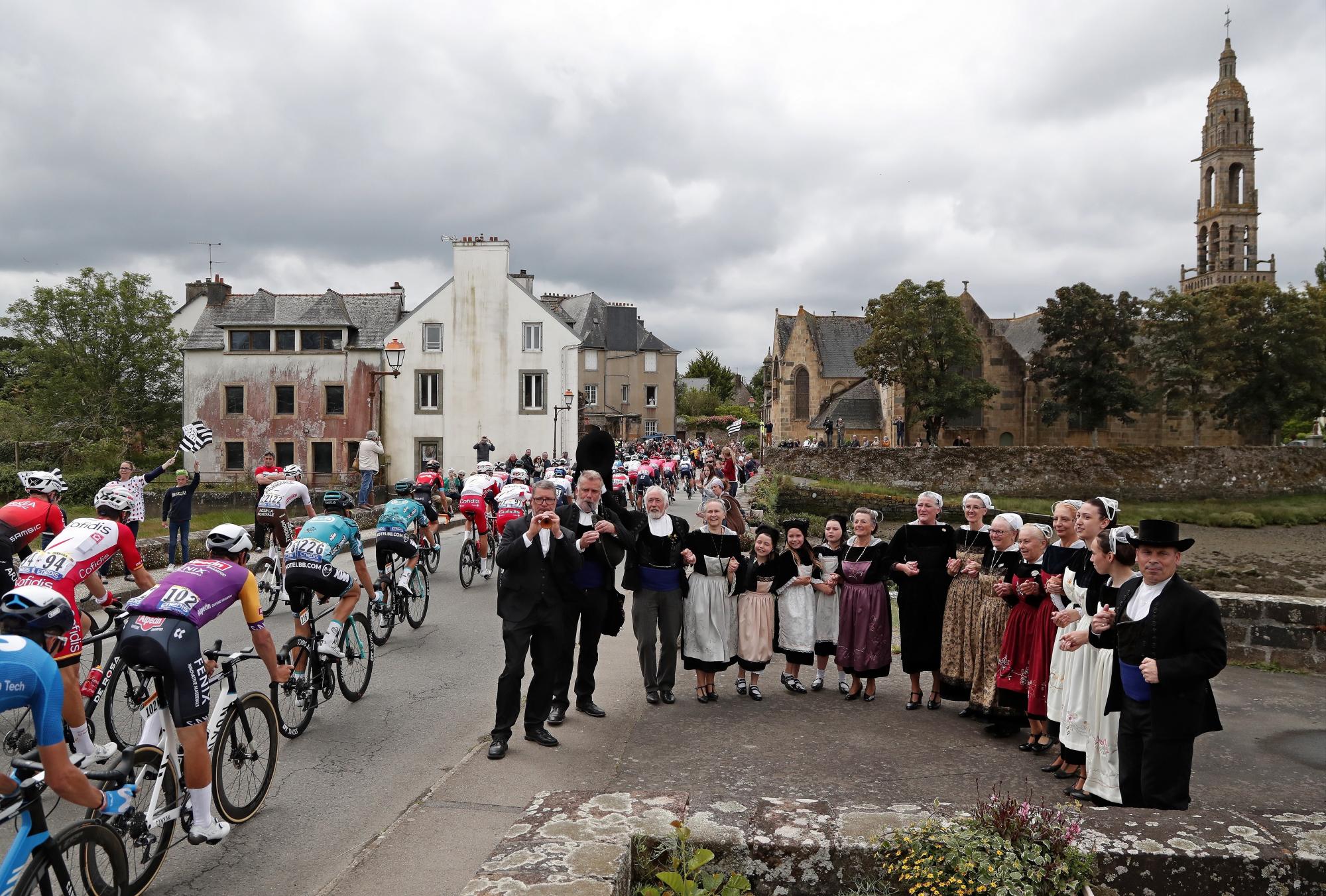 Los ciclistas pasan junto a aldeanos vestidos con trajes tradicionales que interpretan una canción durante la primera etapa del Tour de Francia 2021, a más de 197,8 km de Brest a Landerneau, Francia, el 26 de junio de 2021. (EFE/EPA/Guillaume Horcajuelo)