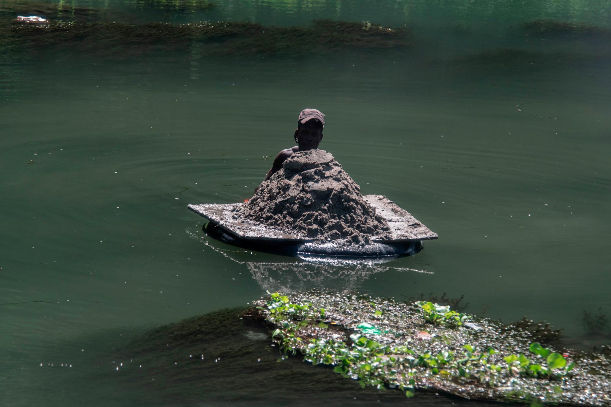 Un hombre extrae arena fina desde el fondo del río y la transporta sobre las aguas.