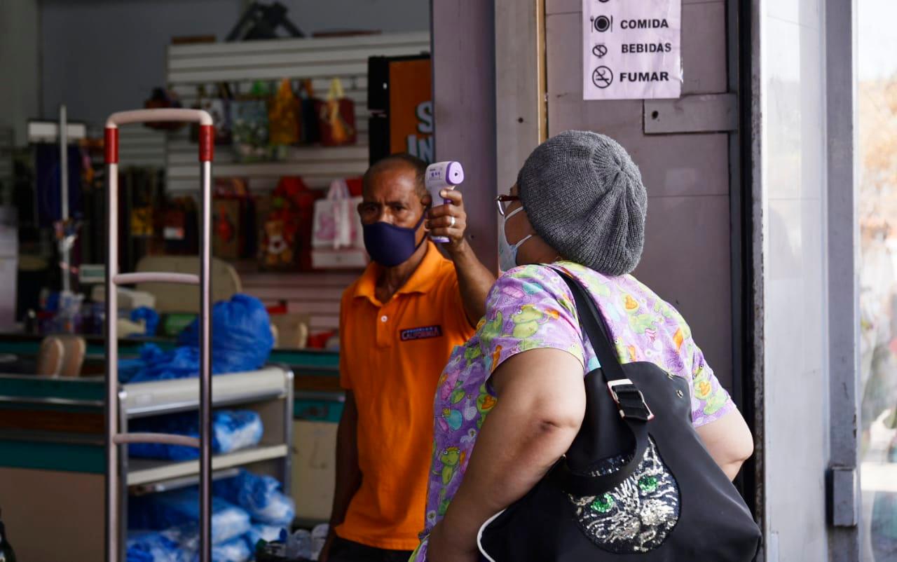 Un empleado revisando la temperatura de una mujer antes de entrar a la tienda.
