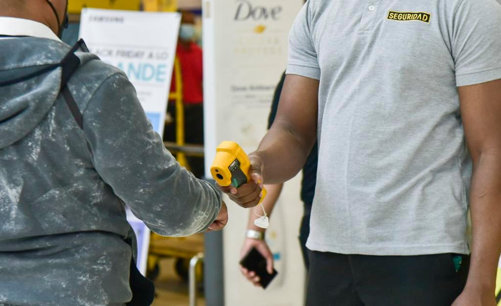 Un empleado toma la temperatura a un cliente previo a permitirle la entrada a un establecimiento.