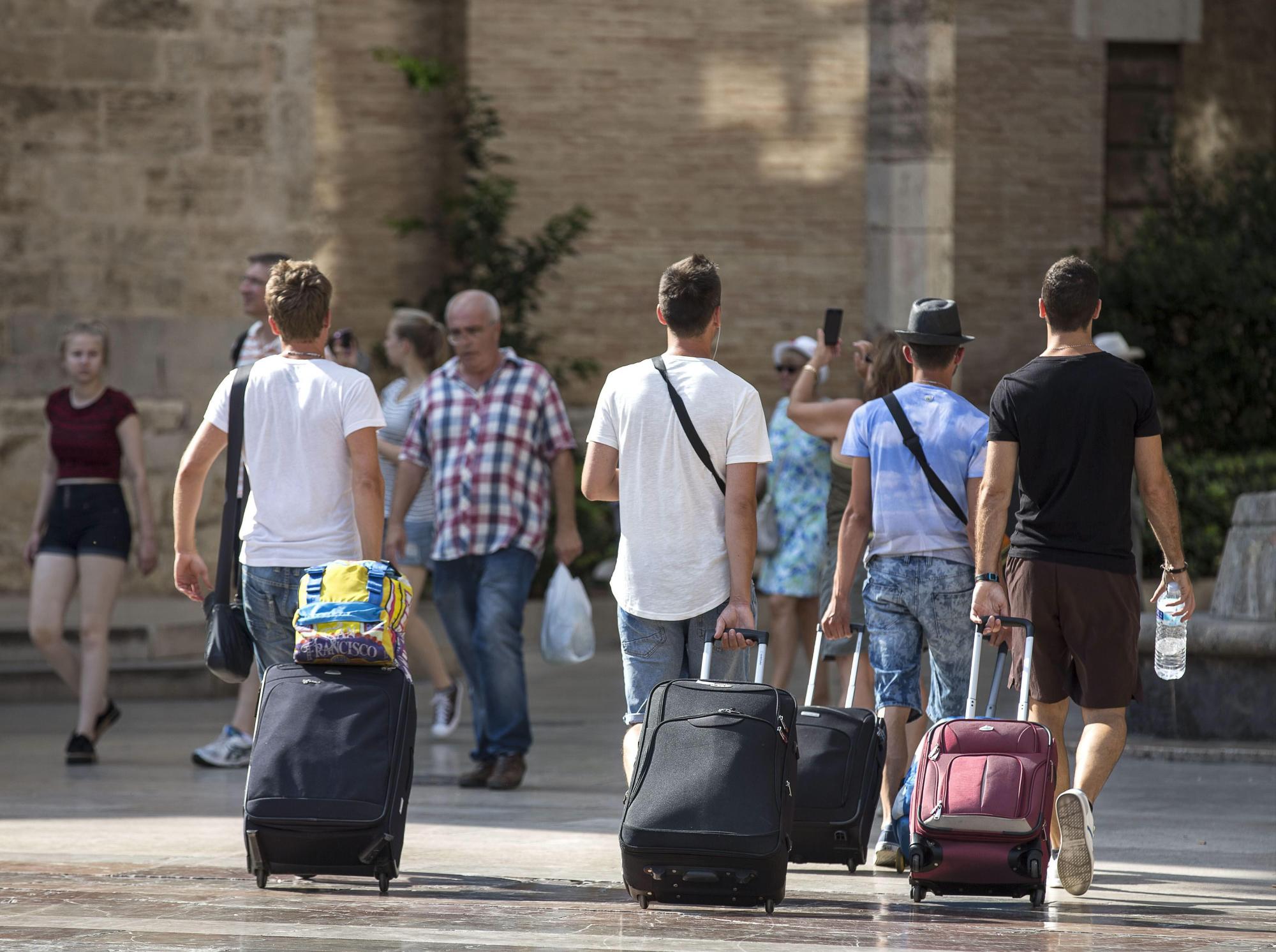 Cuatro jóvenes turistas caminan con su maletas, este mediodía, por la plaza de la Virgen de Valencia. 