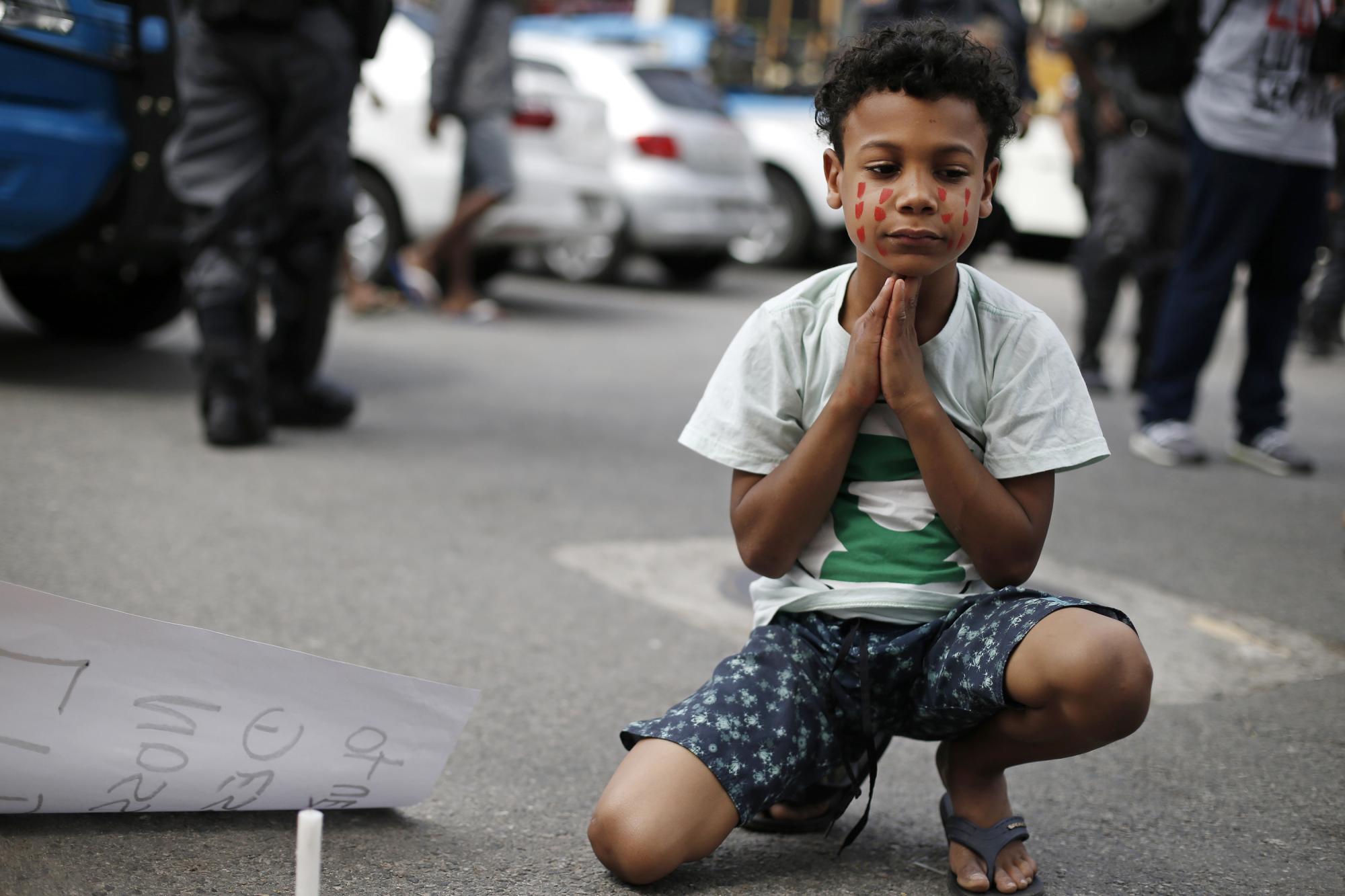 En esta imagen del sábado 22 de agosto de 2015, un chico con el rostro pintado de rojo para simbolizar lágrimas participa en una protesta contra la policía y los conflictos de pandillas que han dejado atrapados en el fuego cruzado a los vecinos de la favela Complexo de Alemao en Río de Janeiro, Brasil.