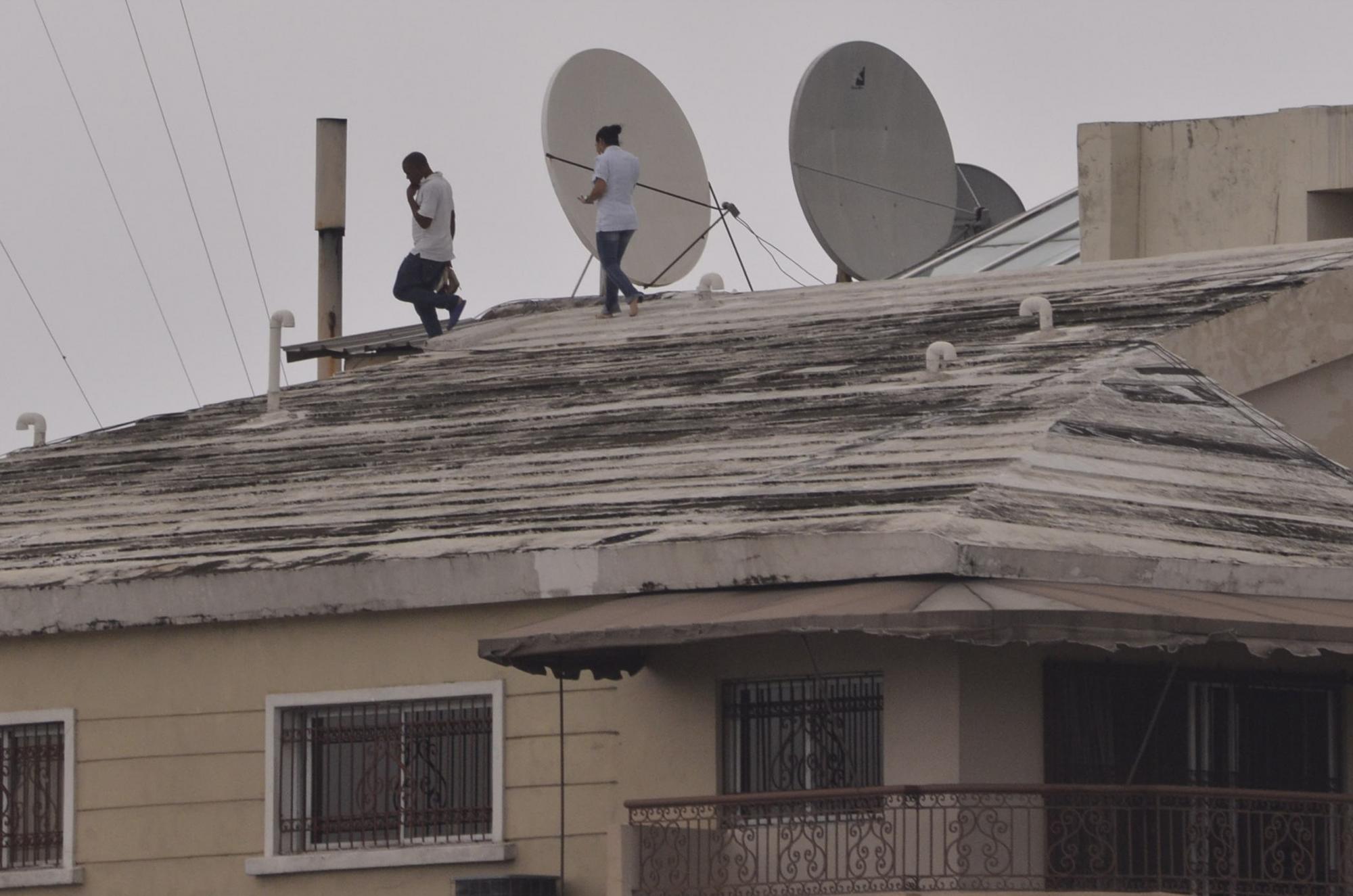 Personas caminan sobre el techo de una vivienda para asegurar los objetos ante el paso de la tormenta tropical Erika.
