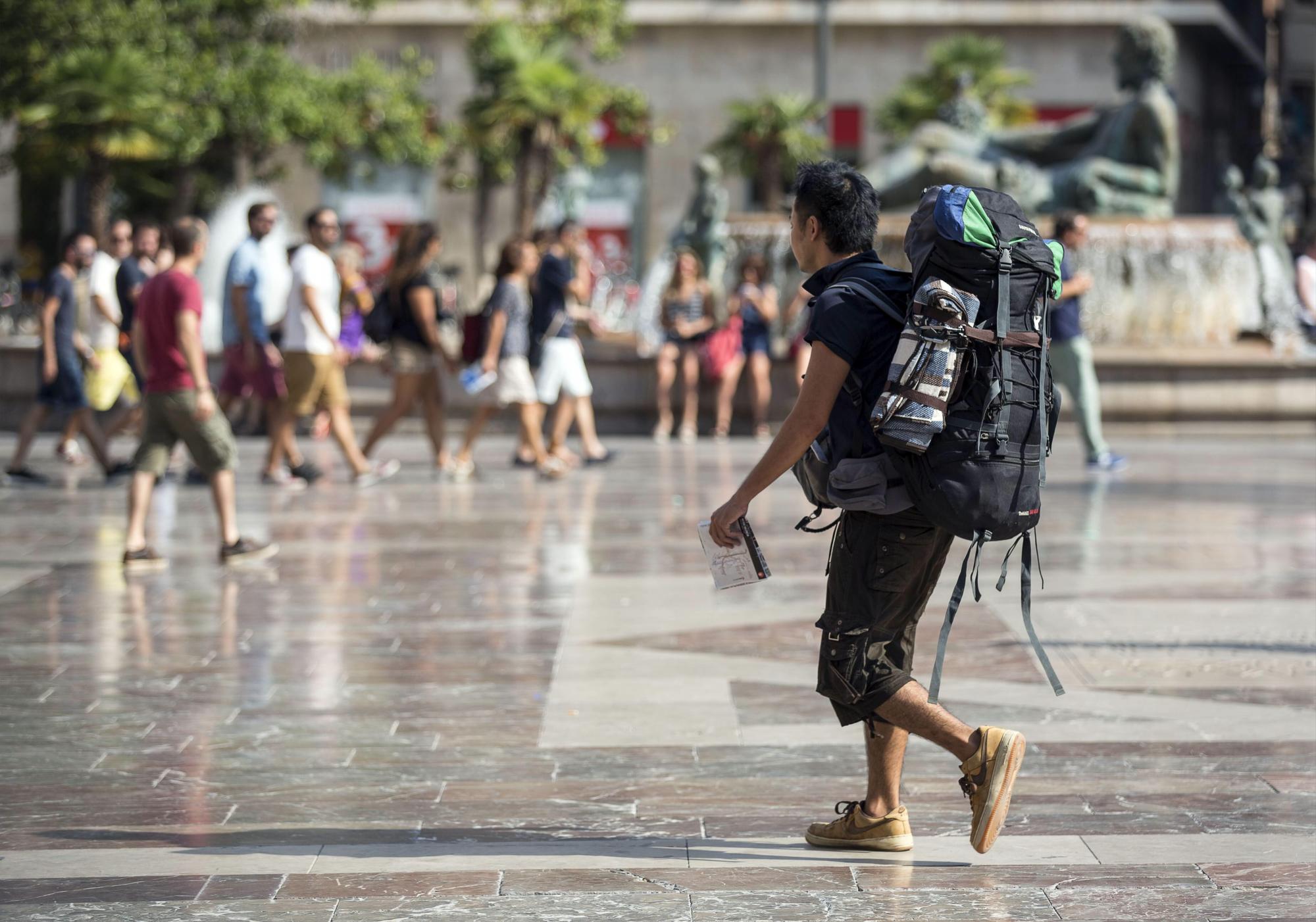 Un viajero con mochila camina por la plaza de la Virgen de Valencia. 