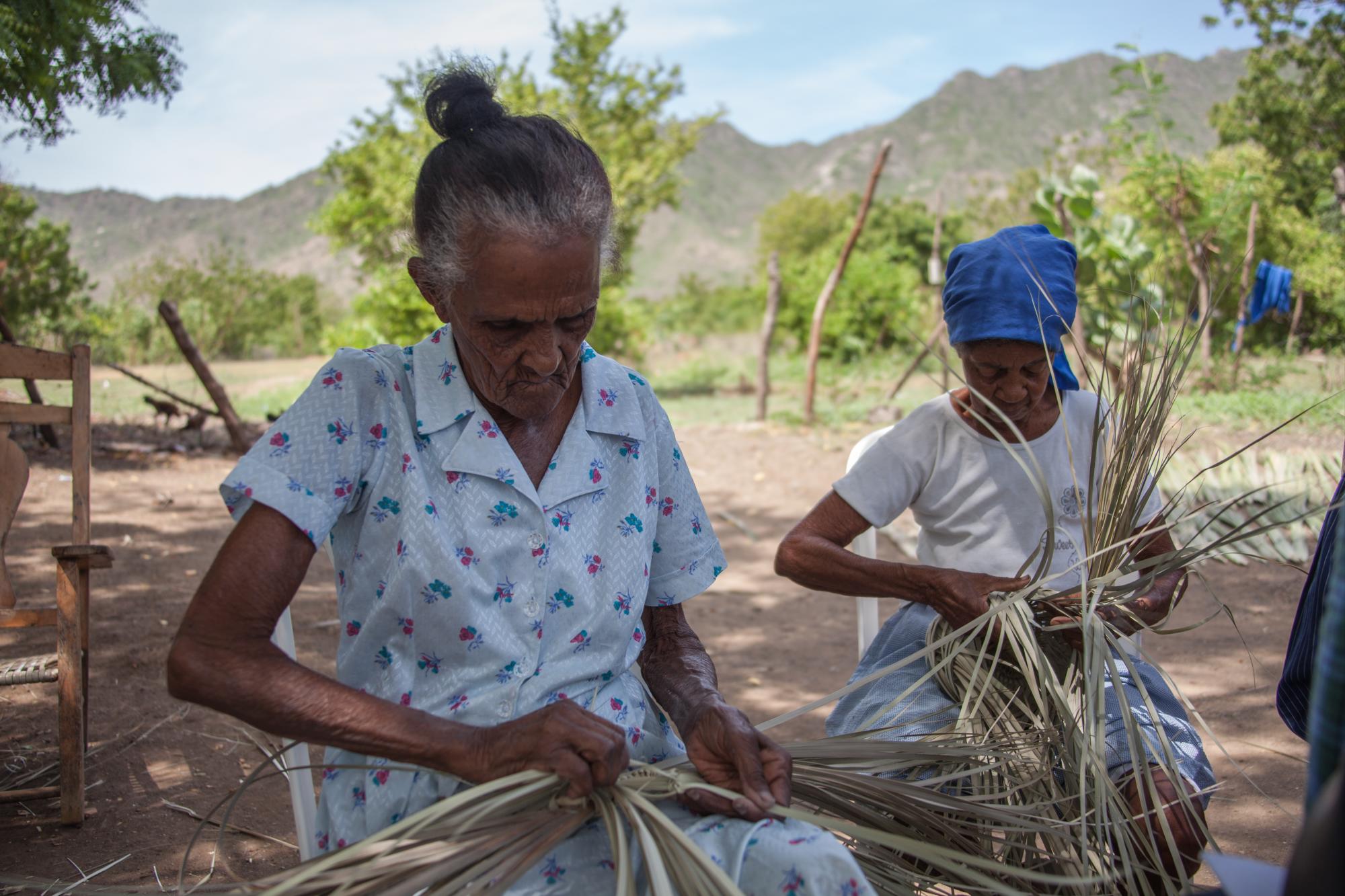 Providencia Lara y Rafaela Antonia Martínez tejen un macutos con ramas de guano.