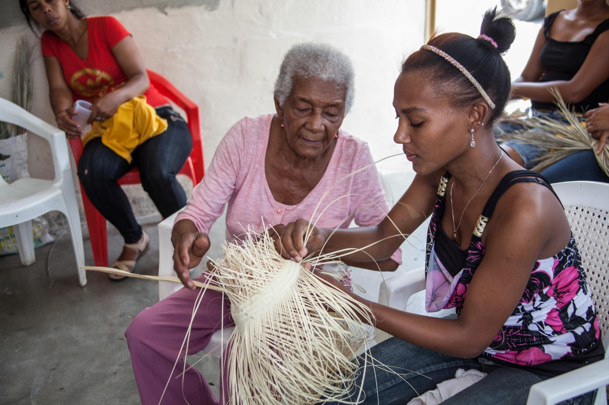 Mélida Villar enseña a Darlenis Pimentel cómo se hacen los sombreros de cana.
