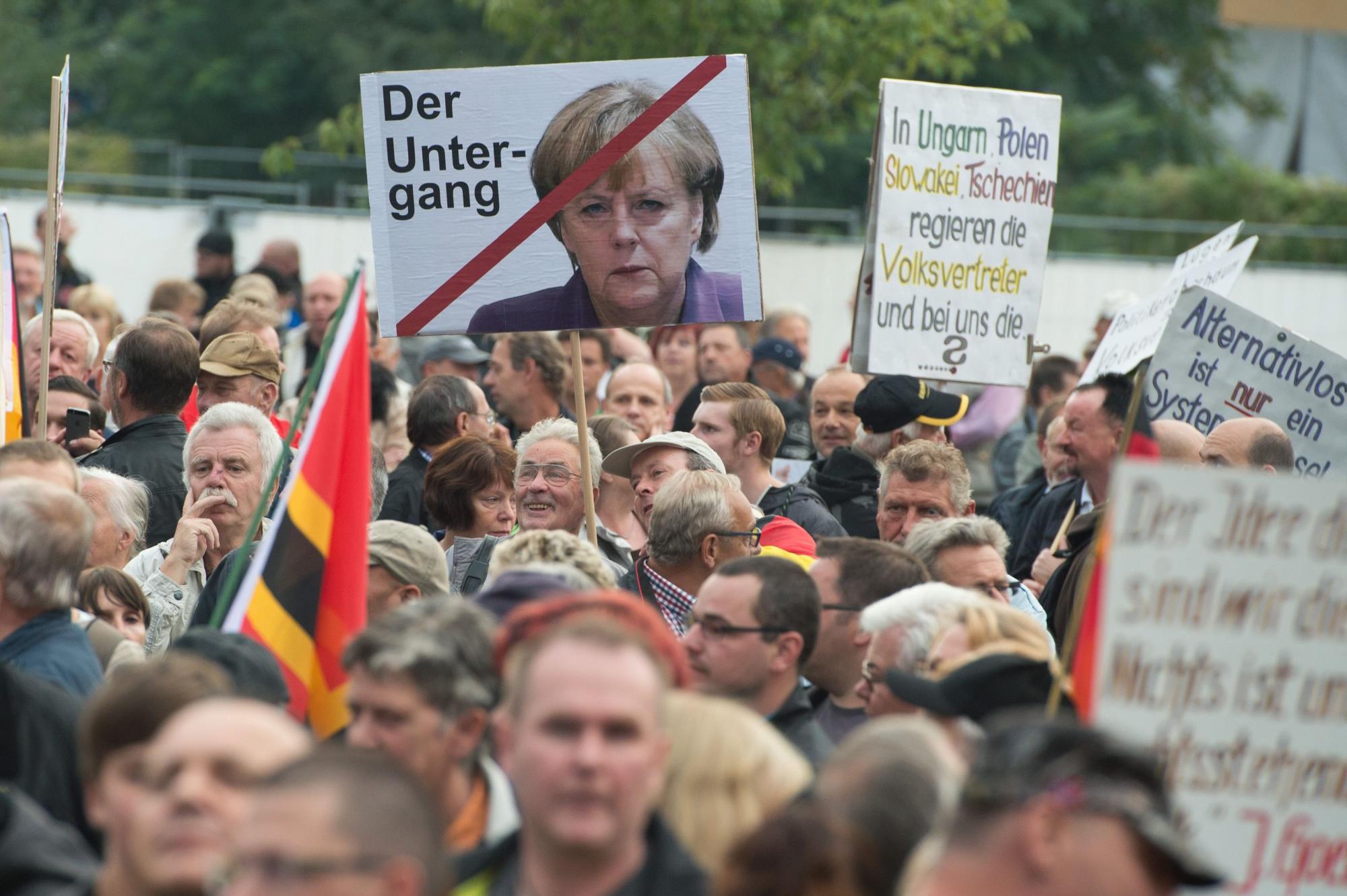 Integrantes y afines al movimiento Patriotas Europeos contra la Islamización de Occidente (PEGIDA) protestan con carteles y banderas (la pancarta con la fotografía de la Canciller alemana Ángela Merkel dice la caía) en la plaza de Neumarkt en Dresden (Alemania),el pasado 14 de septiembre de 2015.  