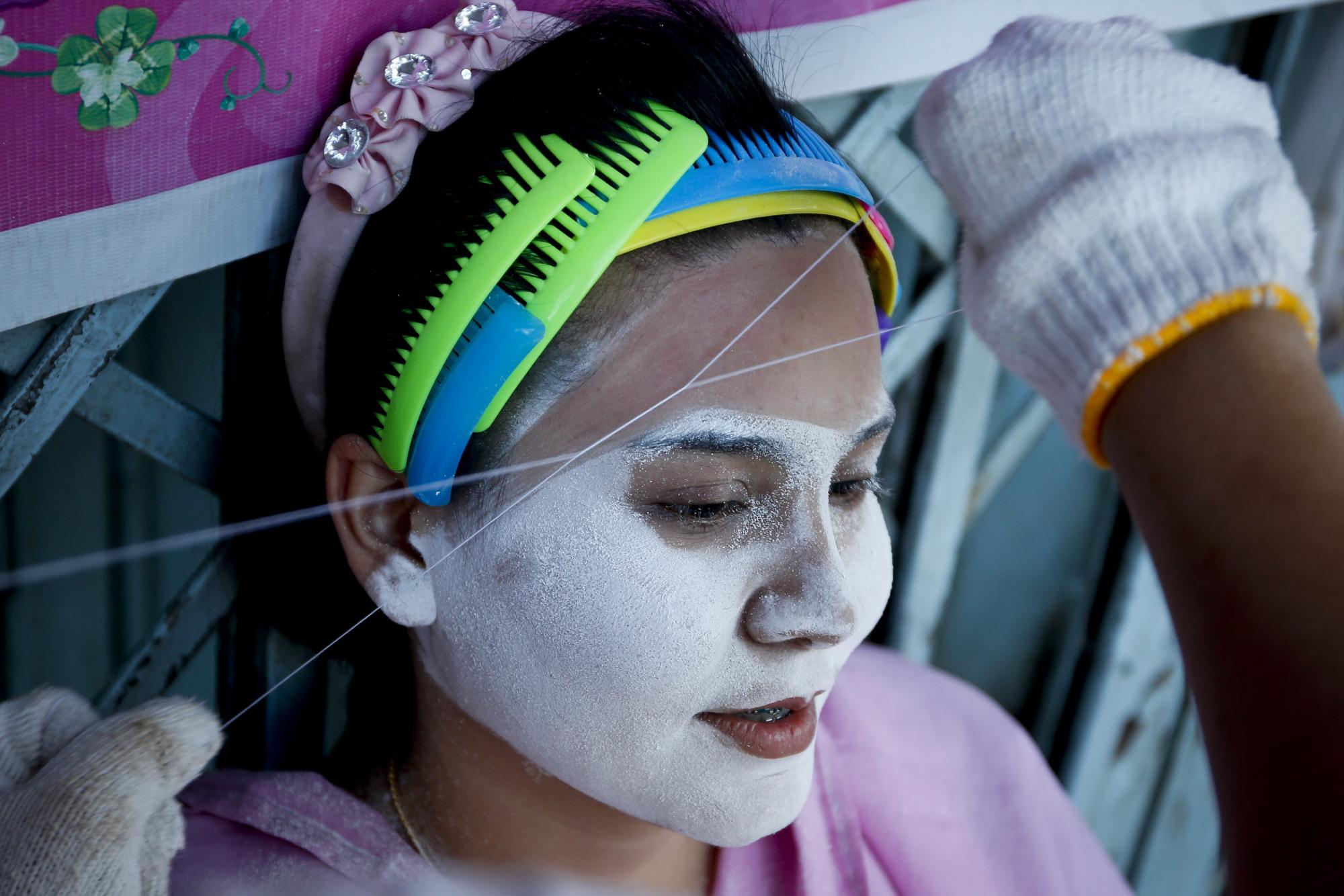 Una chica recibe el tratamiento de los hilos entrecruzados para remover el vello facial en una sala de belleza en Chinatown en Bangkok (Tailandia).