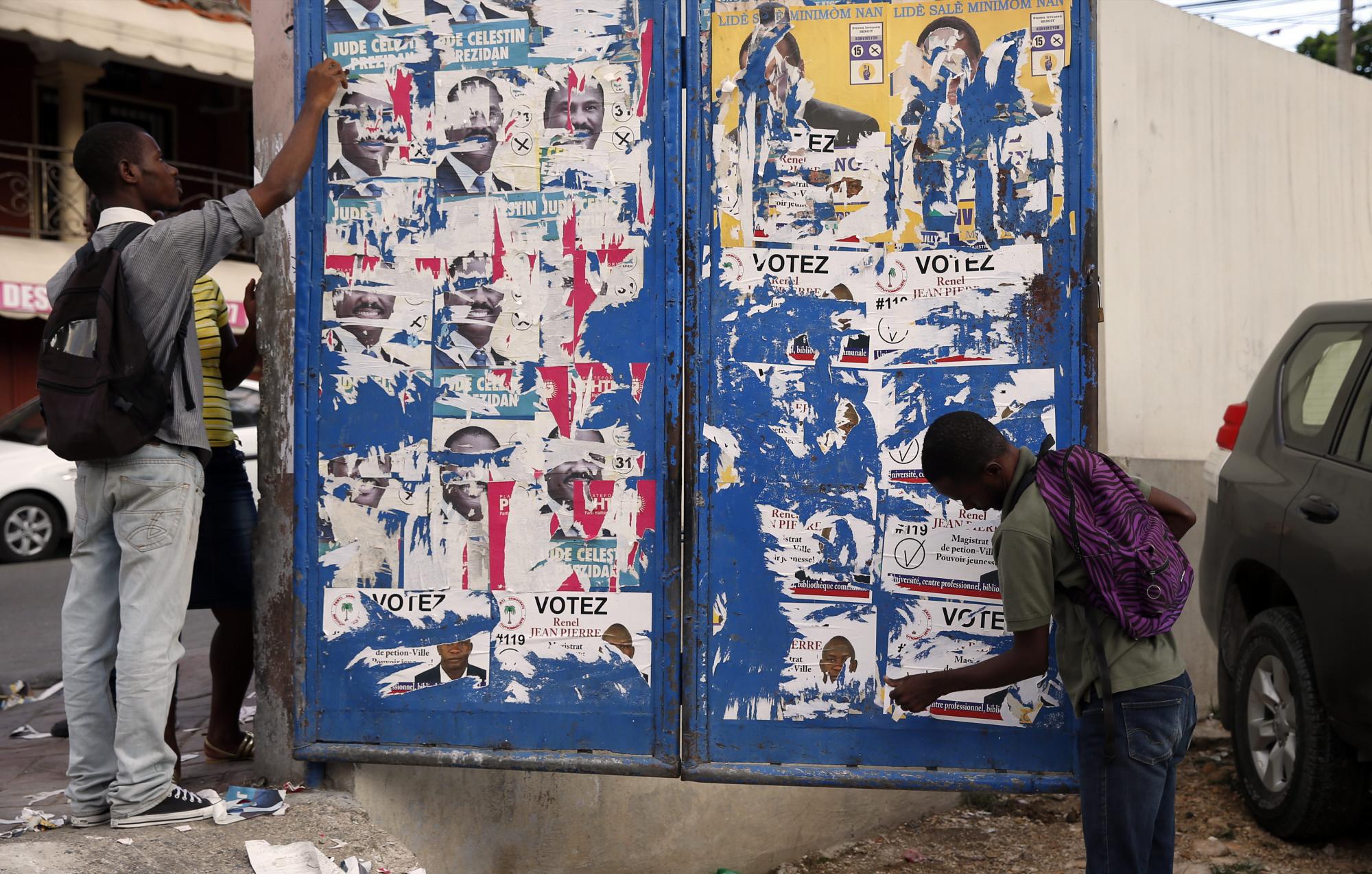 Jóvenes retiran publicidad electoral en la entrada de un centro de votación hoy.