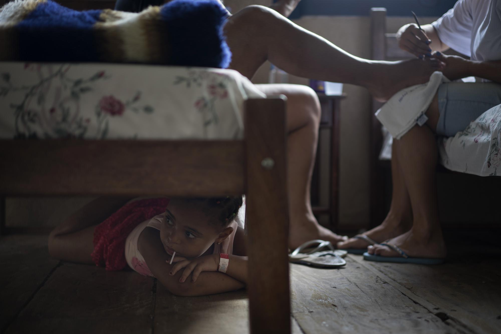 En esta imagen, tomada el 9 de noviembre de 2015, la pequeña Nicole, de cinco años, toma un caramelo debajo de una cama mientras su madre recibe una pedicura en un hotel que acoge a los desplazados por la rotura de una presa, en Mariana, en el estado brasileño de Minas Gerais. La vivienda de Nicole quedó destruida el 5 de noviembre, cuando dos presas de una mina de hierro se rompieron inundando Bento Rodrigues, una localidad en el sureste de Brasil.