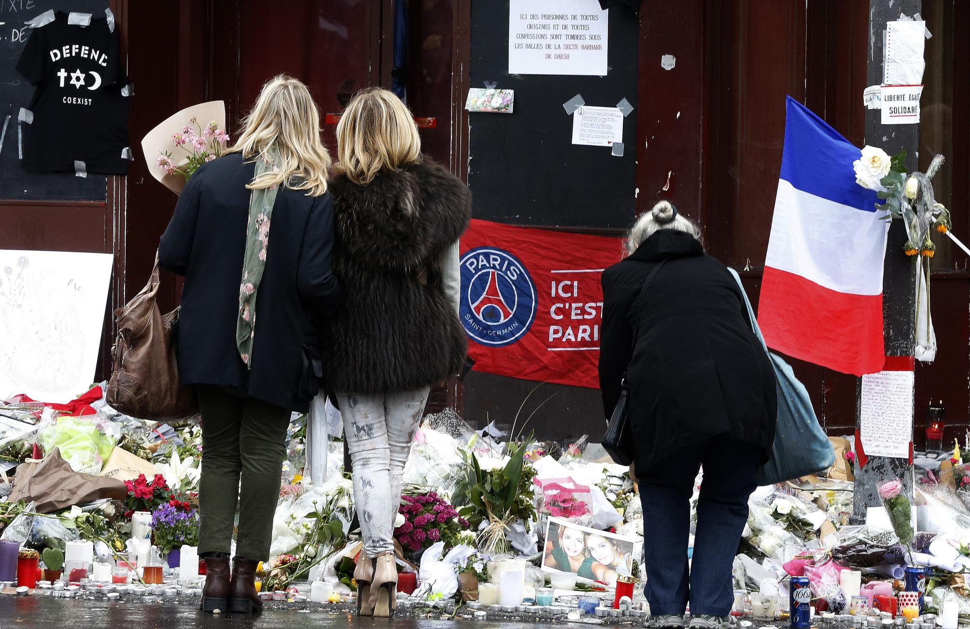 Unas personas ven las rlores, regalos y velas colocados afuera del restaurante Le Carillon en París, el jueves 19 de noviembre de 2015 en memoria de los ataques del viernes pasado que dejaron 129 muertos en varios puntos de la capital Francesa.