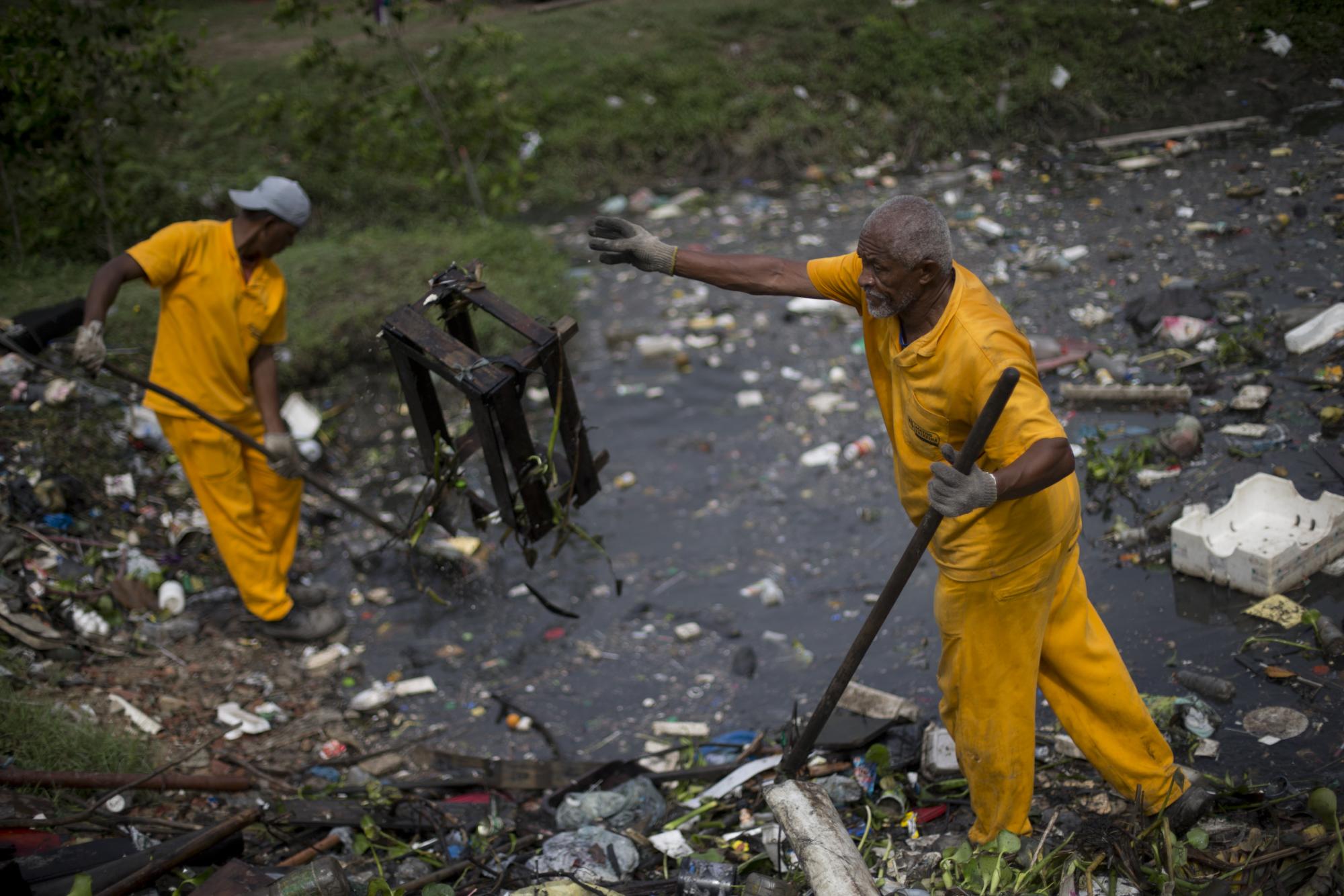 En esta imagen, tomada el 5 de noviembre de 2015, dos operarios retiran basuras recogidas por barreras flotantes en el río Meriti, que desemboca en la bahía Guanabara, en Río de Janeiro, Brasil. Una nueva ronda de estudios y análisis realizados por The Associated Press indicó la presencia de patógenos incluso en aguas alejadas de la costa, donde desembocan ríos fétidos con aguas residuales y desagües de tormentas. 