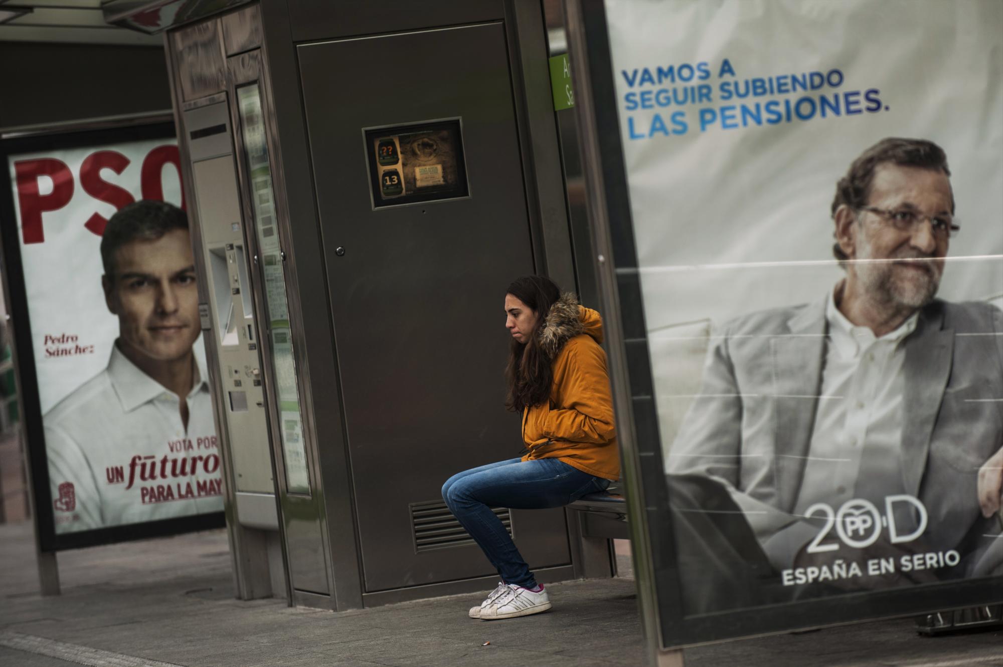 En esta imagen, tomada el 8 de diciembre de 2015, una joven espera en una parada de autobús con carteles electorales del líder del partido Popular, Mariano Rajoy (derecha) y del Partido Socialista, Pedro Sánchez, antes de las elecciones generales del 20 de diciembre, en Vitoria, em el norte de España. Las encuestas muestran que el Partido Popular del presidente Mariano Rajoy será el más votado, aunque no obtendría los apoyos necesarios para conservar la abrumadora mayoría que tiene en el Parlamento _ lo que supondría que tendría que asociarse con otra formación, probablemente Ciudadanos. Otra posibilidad podría ser una coalición entre los socialistas y Podemos.