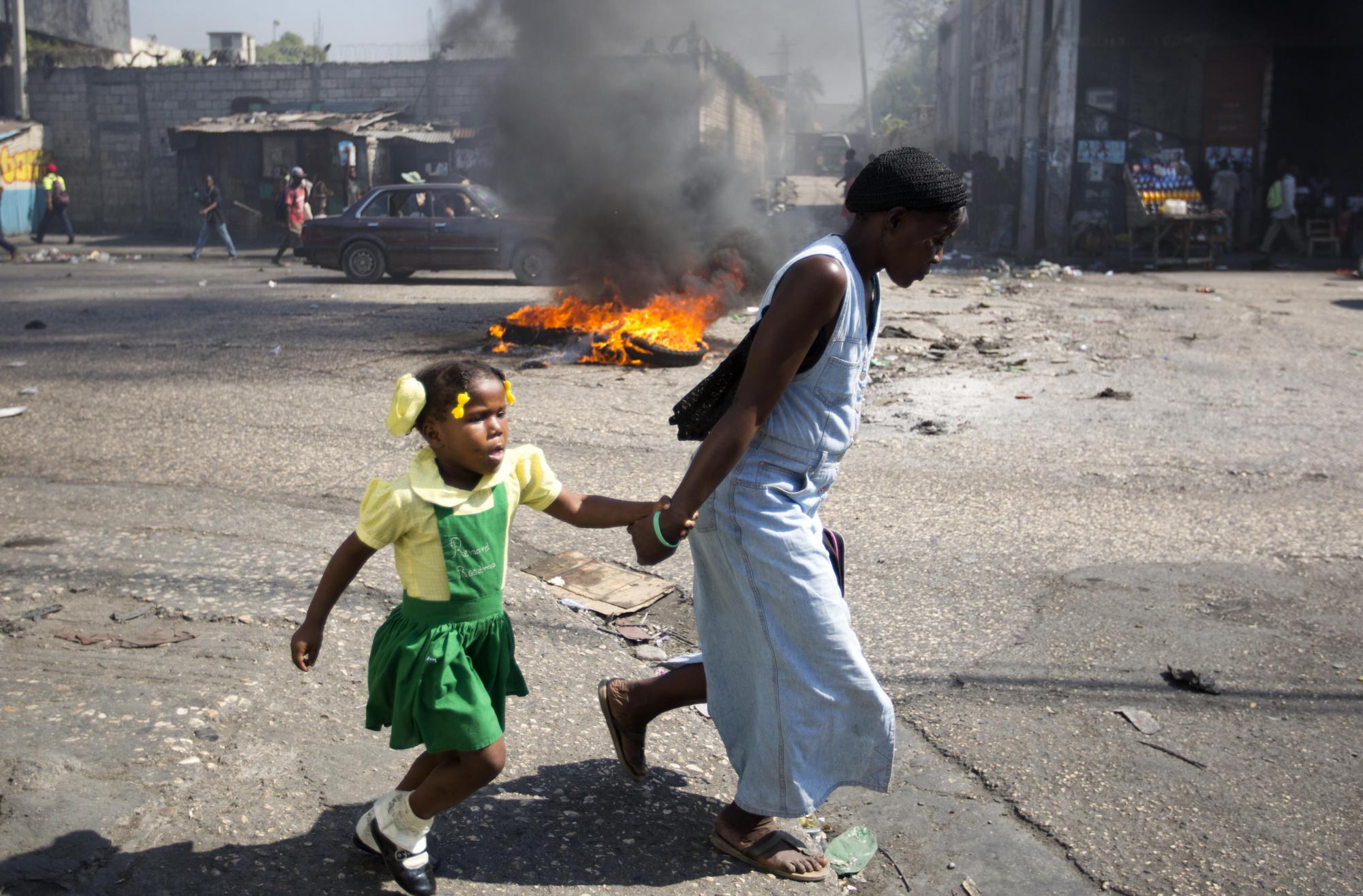 Una mujer y una niña corren frente a una de las barricadas durante la protesta en Puerto Príncipe.