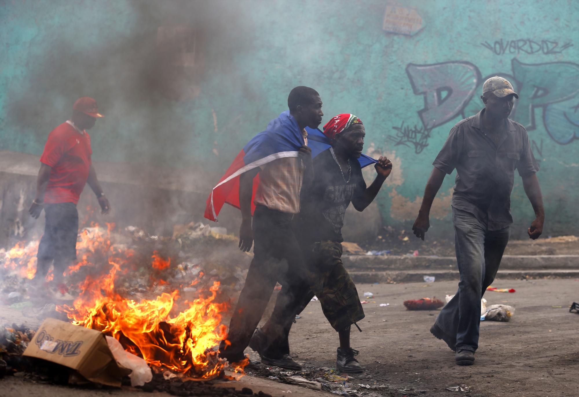 Manifestantes pasan junto a una barricada durante la marcha organizada por la oposición hoy viernes 22 de enero de 2016, en Puerto Príncipe.