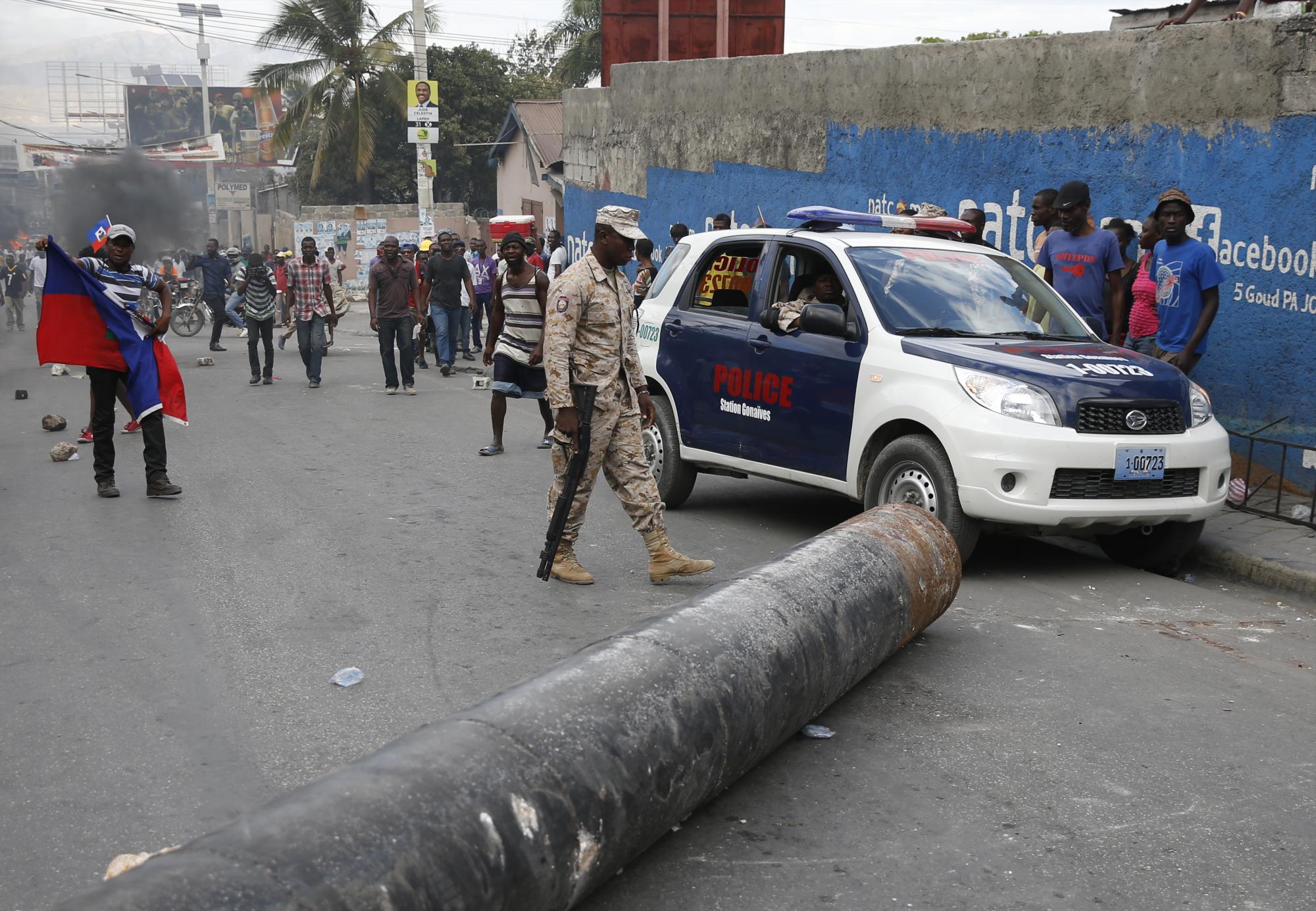 Policías y manifestantes pasan junto a una barricada durante la marcha organizada por la oposición el viernes 22 de enero de 2016, en Puerto Príncipe (Haití).