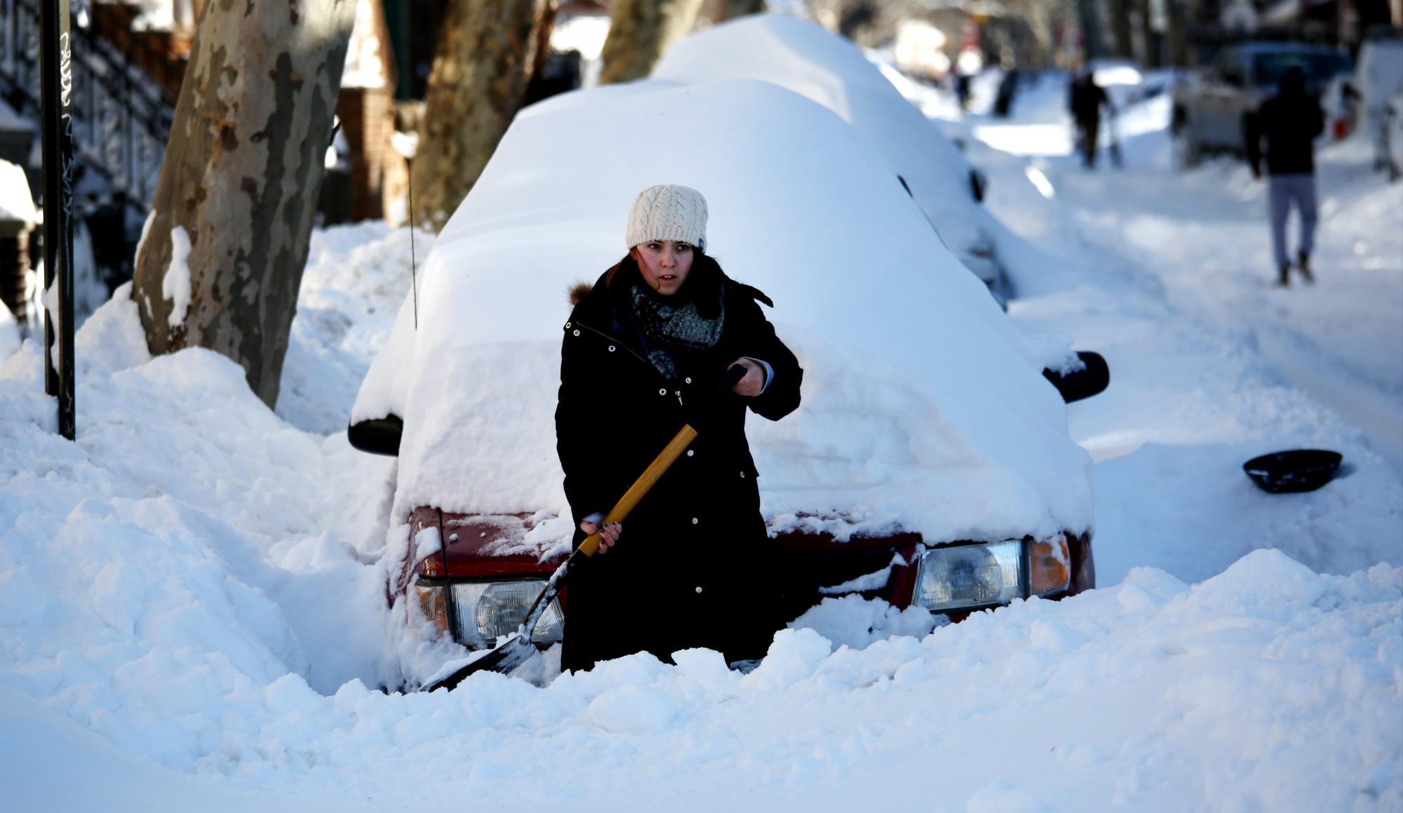 Una mujer limpia la nieve que cubre su auto en Brooklyn
