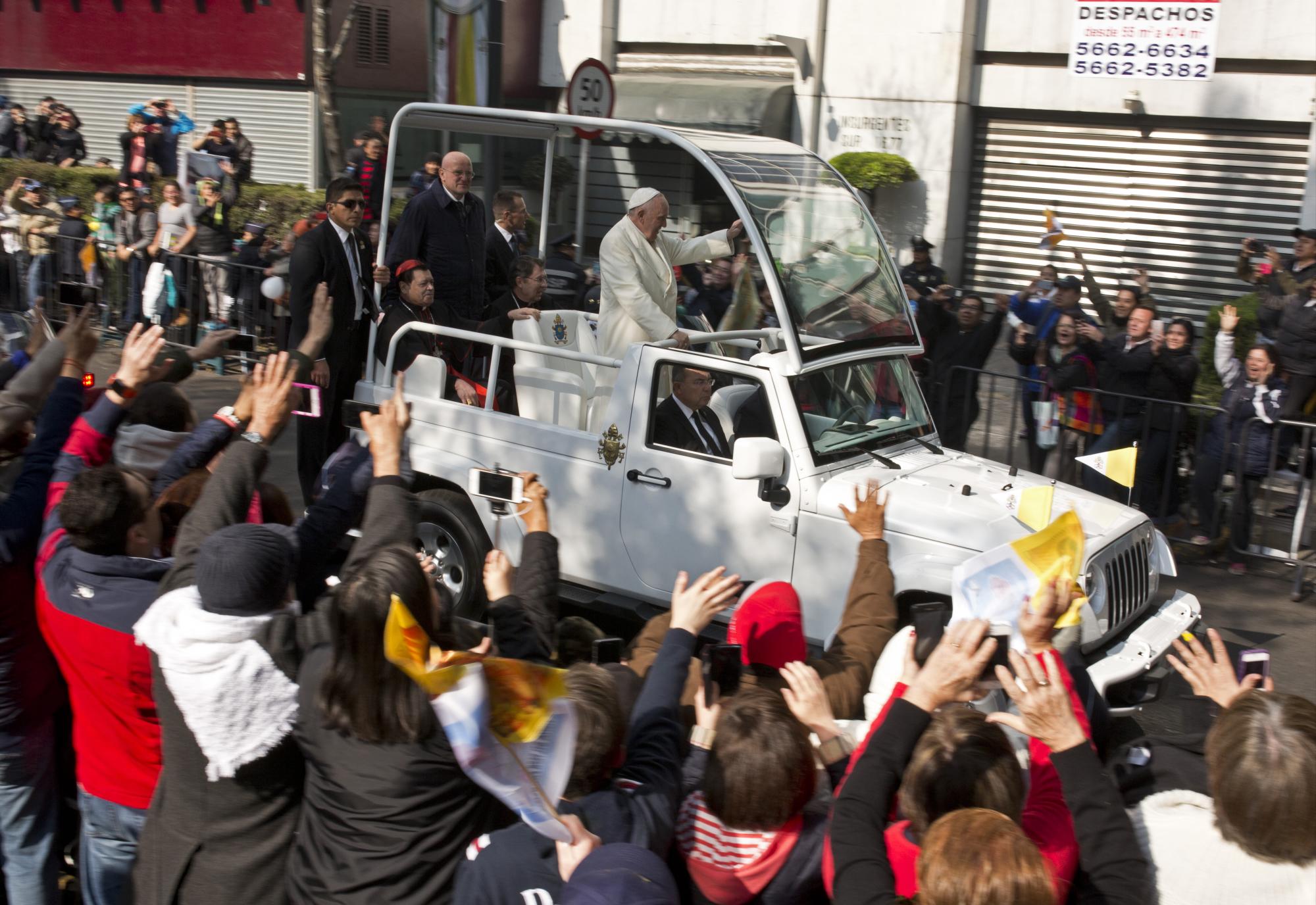 Las personas saludan al papa Francisco a su paso en el papamóvil por las calles de la Ciudad de México.