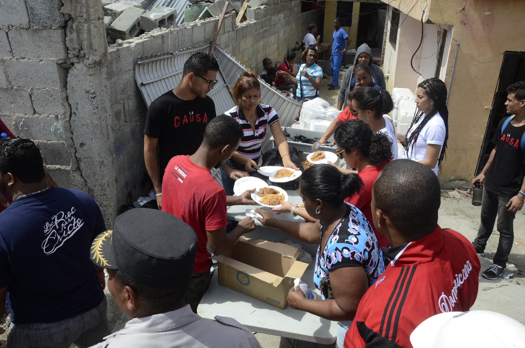 Varias personas afectadas por la explosión de la planta de gas esperan que le sirvan alimentos donados por el grupo Juventud por una Misión.