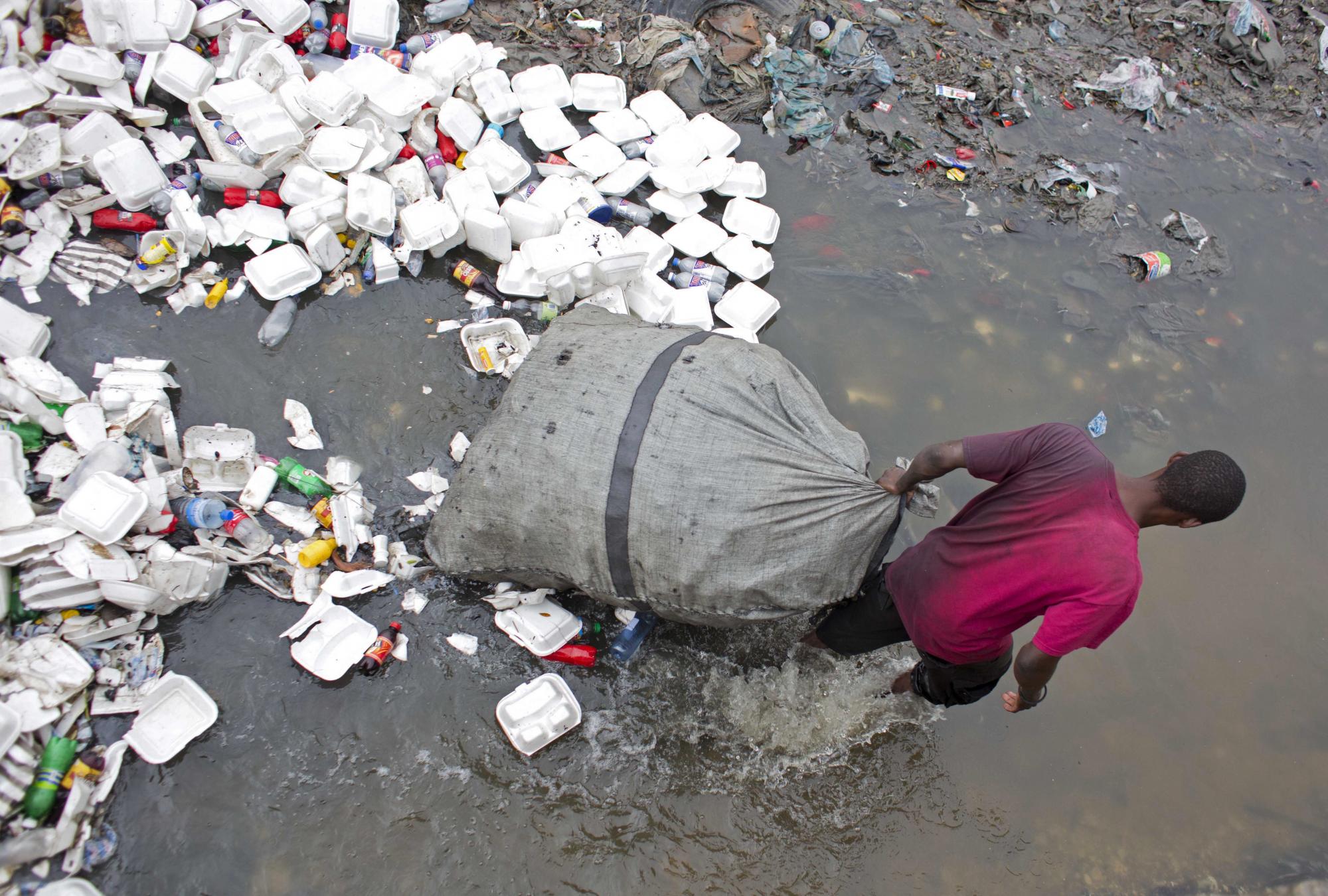 Un hombre camina por aguas llenas de basura arrastrando la bolsa en la que lleva las botellas vacías que luego venderá en el centro de Puerto Príncipe.