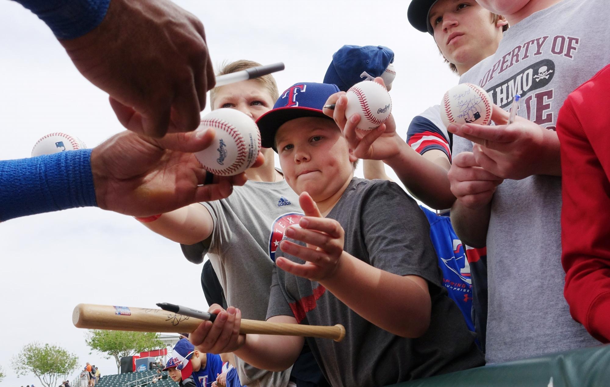 Ian Desmond, quien firmó por un año con Texas, aprovecha para firmar bolas a los niños en Surprise, Arizona.