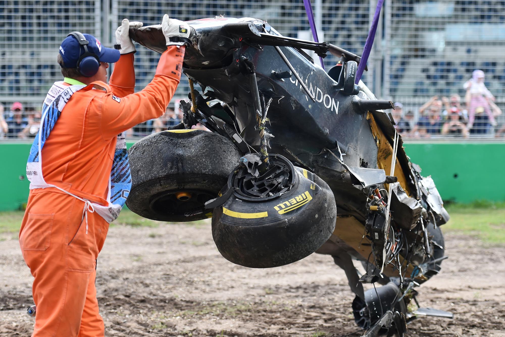 Un asistente de la pista ayuda a remover el desfigurado automóvil de Fernando Alonso. 