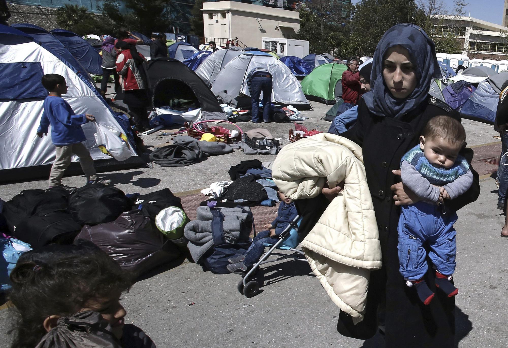Una mujer sostiene a su bebé en brazos junto a unas tiendas de campaña en el Puerto del Pireo en Grecia hoy, 31 de marzo de 2016. 