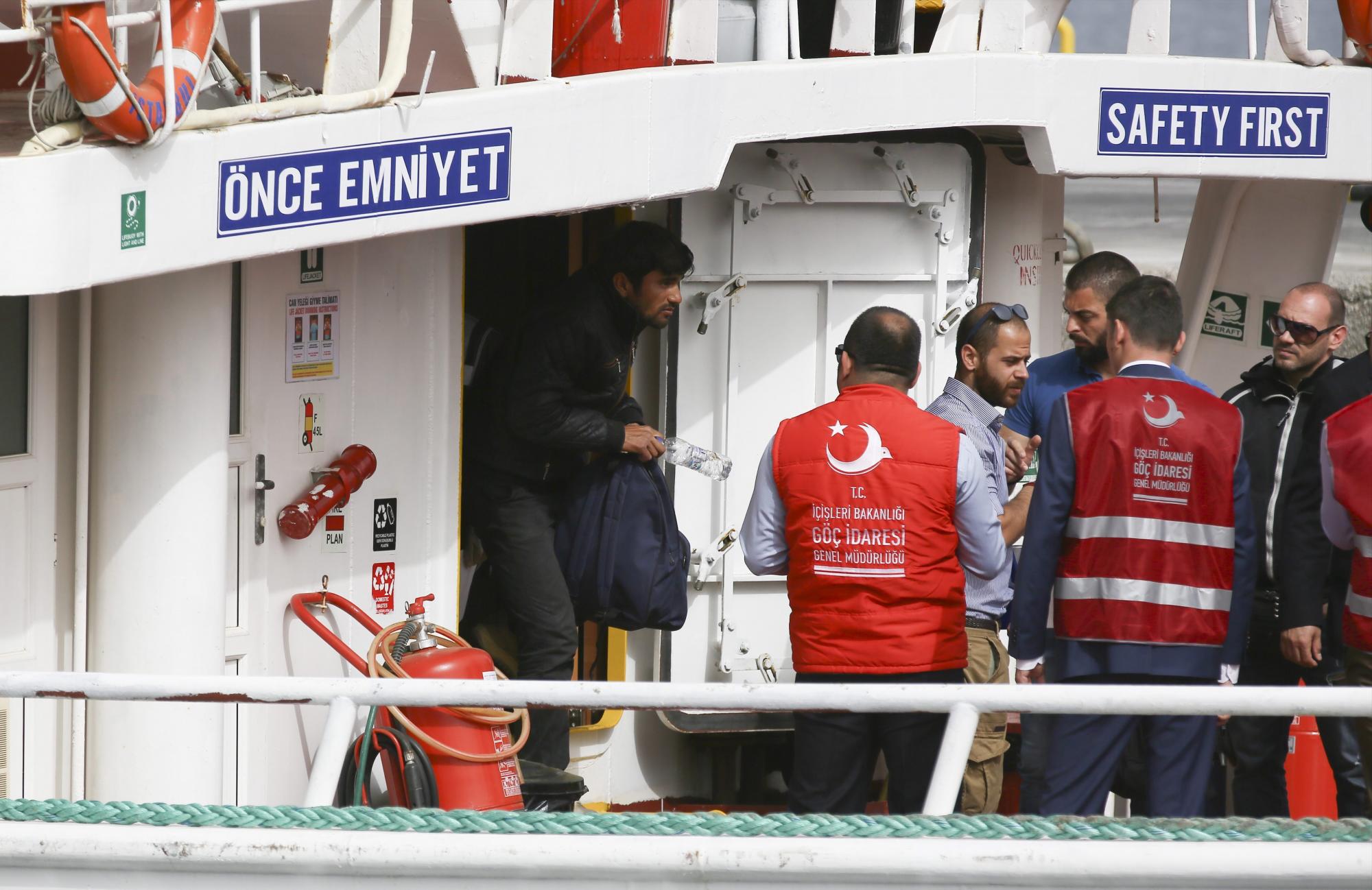 Policías turcos escoltan a los refugiados que fueron deportados desde la isla griega de Lesbos, a su llegada en barco a Izmir, Turquía. 