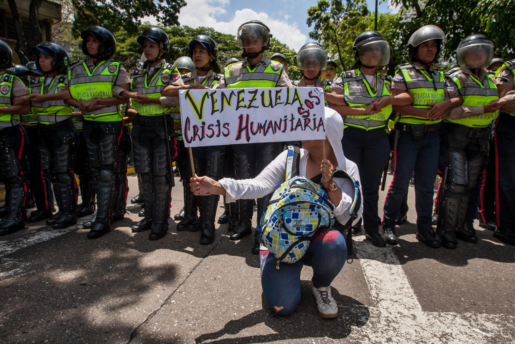 Una manifestante sostiene un letrero con la frase Venezuela s.o.s. crisis humanitaria, frente a miembros de la Policía Nacional Bolivariana (PNB)
