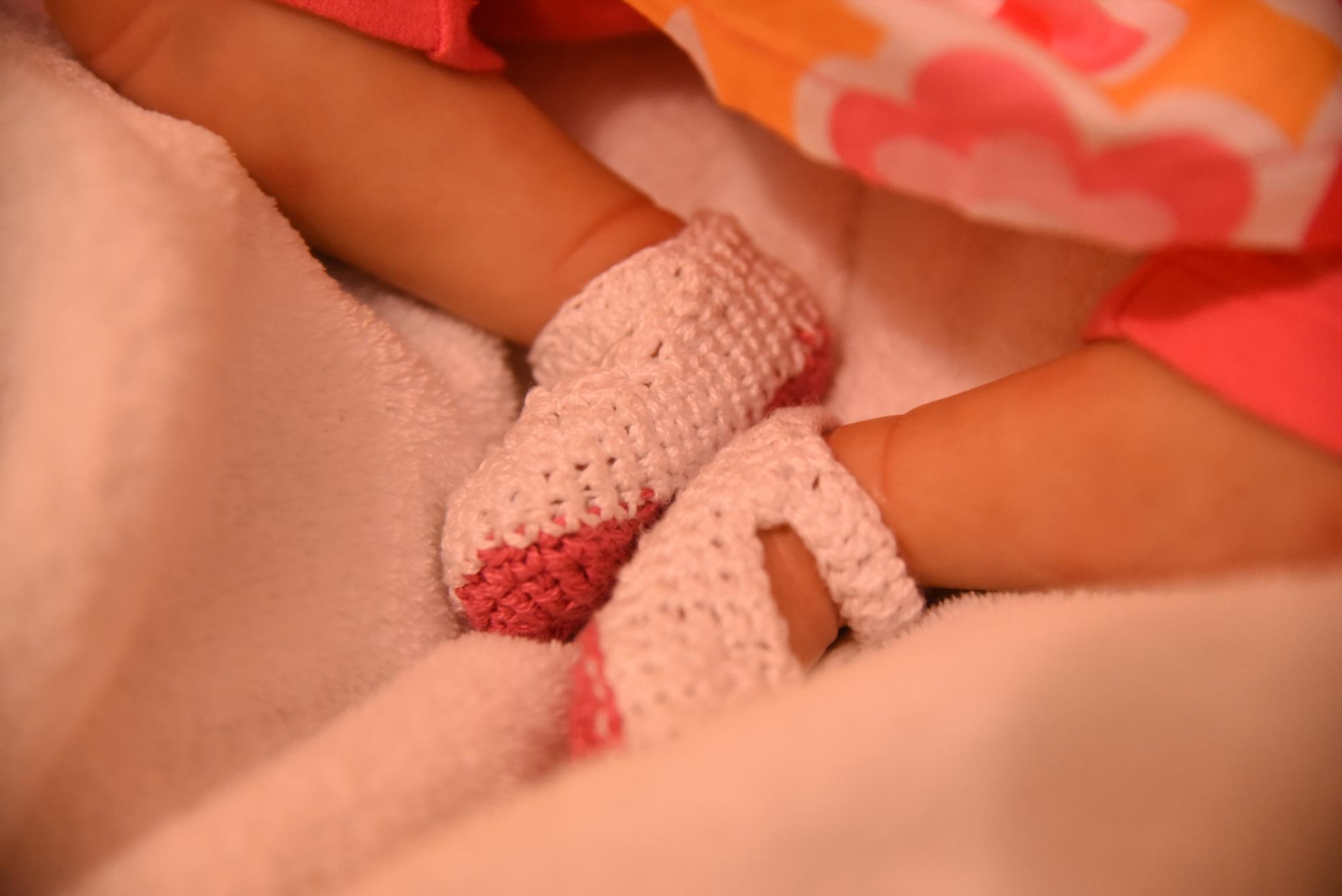 Detalle fotográfico de los pies de una muñeca recién nacida con zapatos tejidos.