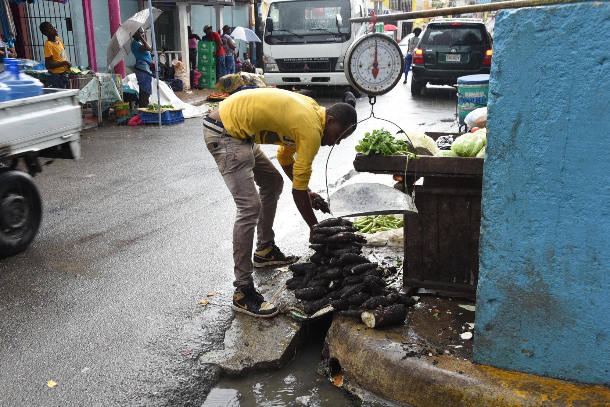 Un comerciante amontona yucas sobre un paso de aguas negras.