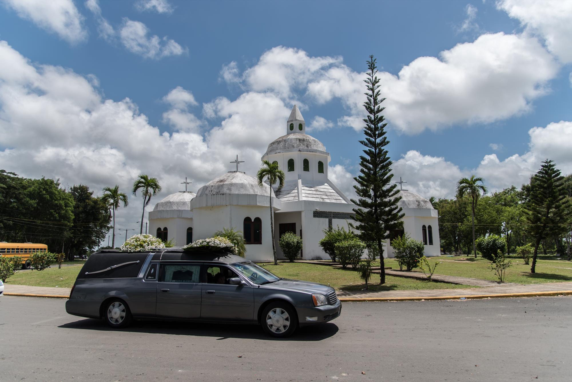Un carro fúnebre pasa frente a la iglesia del cementerio.