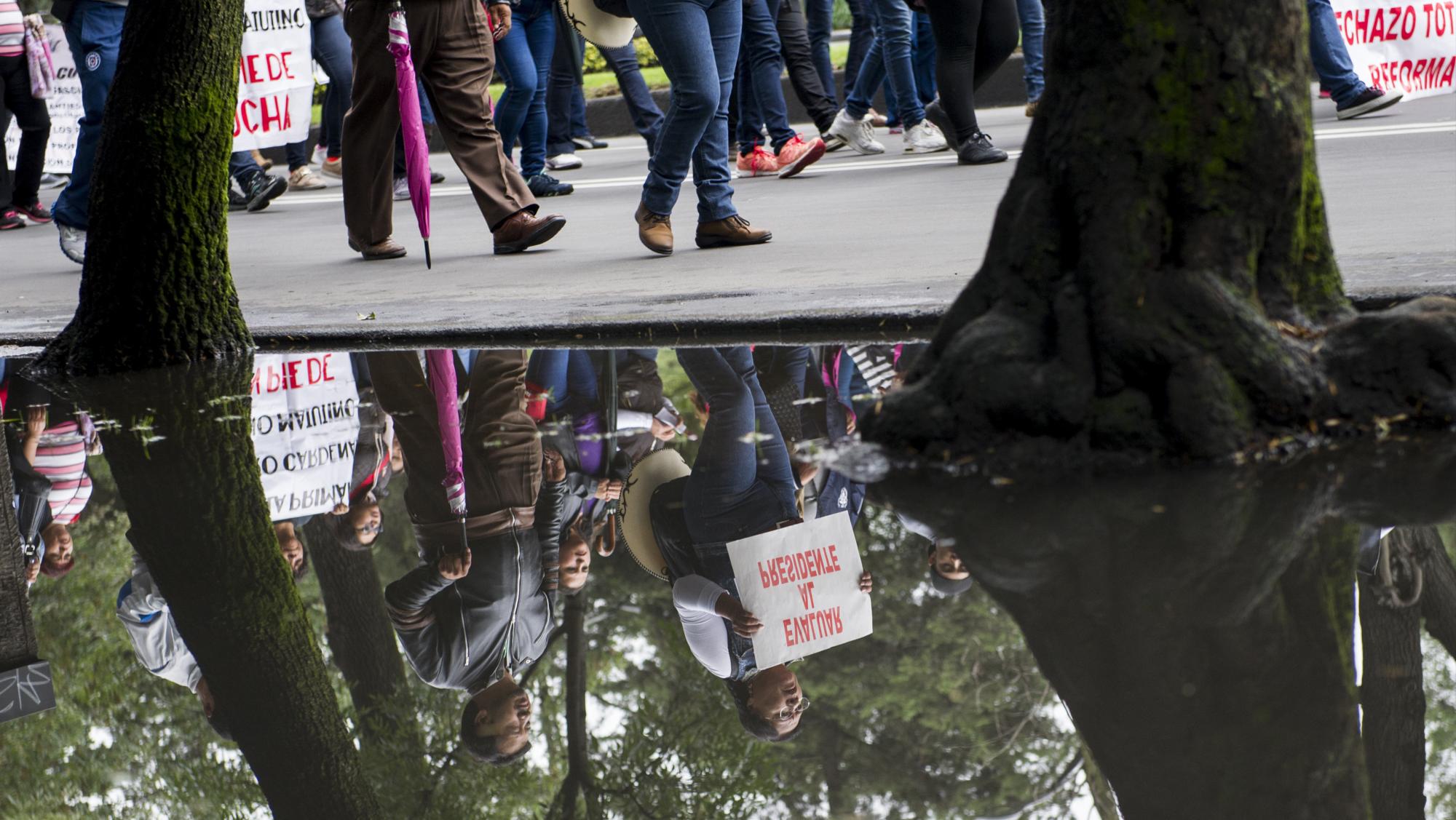 En esta imagen, tomada el 11 de julio de 2016, el reflejo de un manifestante, perteneciente a un sindicato de profesores, se proyecta en un charco mientras marcha con un cartel con el lema “Evalúen al presidente”, en la ciudad de México.