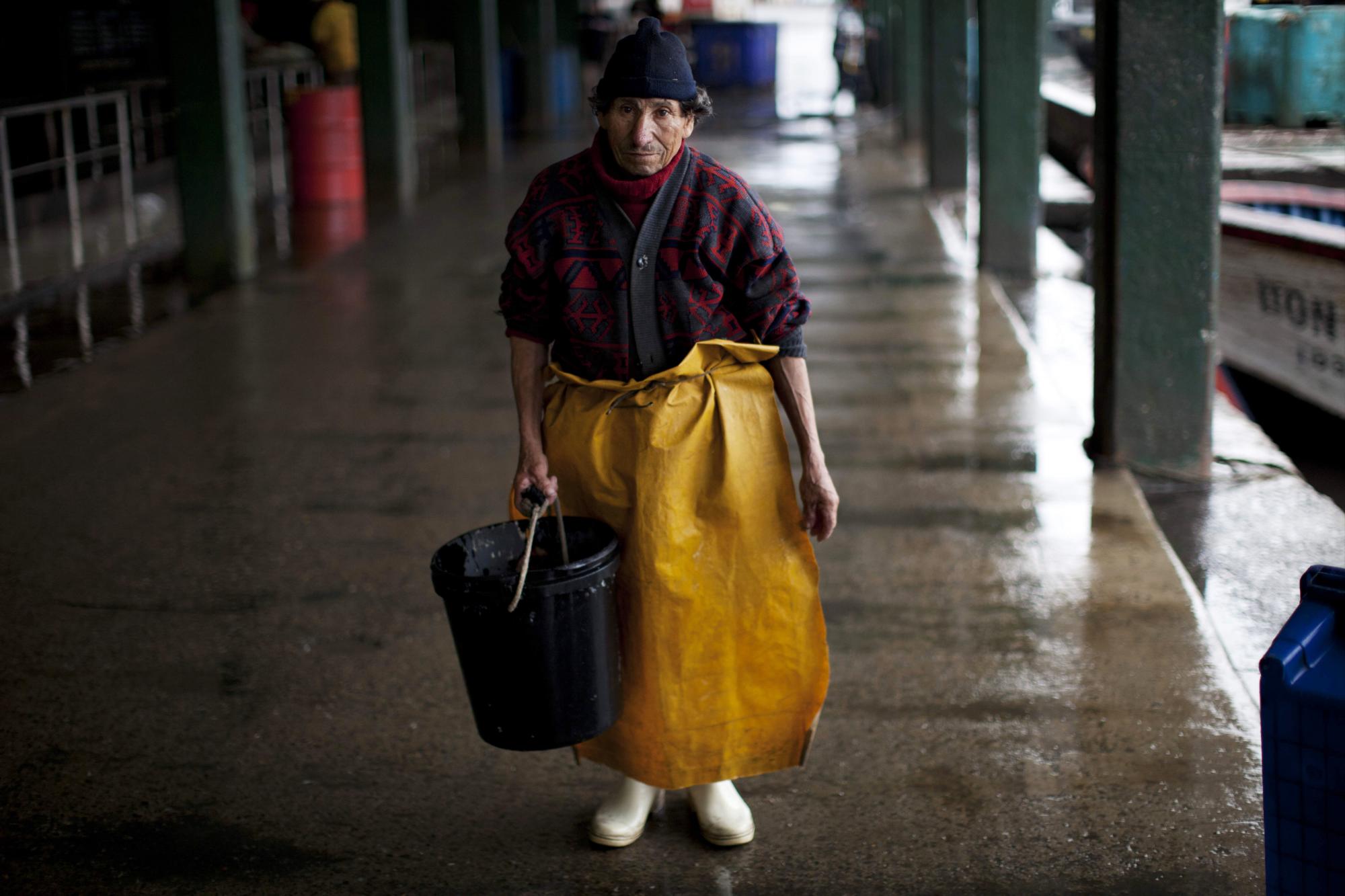 En esta imagen del 27 de noviembre de 2012, Humberto Cova Mendoza, que trabaja escamando pescado, posa para un retrato en el puerto de El Callao, Perú. Muchos creen que la modernización del puerto pueda tener un efecto negativo en su modo de vida, pero a los pescadores también les preocupa que la sobrepesca ha mermado el caladero de pez escorpión, jurel y lisa. Los pescadores llegaban antes a los muelles de El Callao y vendían hasta 110 libras de pescado. Ahora no se ofrecen más de 15 libras.