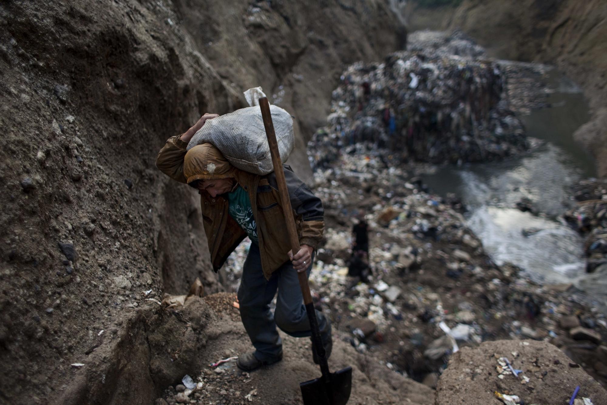 En esta imagen de archivo del 5 de octubre de 2011, un hombre que sólo se identificó como Wilmer carga un saco con metal que recogió tras trabajar un día entero al fondo de uno de los mayores vertederos de la ciudad, conocido como La Mina en Ciudad de Guatemala. Cientos de trabajadores informales descienden cada día por las laderas del basurero y el torrente que llega de un desagüe de tormentas y una cañería al fondo de una garganta, para buscar chatarra que vender. Esta actividad, conocida localmente como minería, es extremadamente peligrosa debido a los deslaves y los colapsos, pero les da a muchos de ellos unos 150 quetzales (20 dólares) al día, casi el doble del salario mínimo diario.