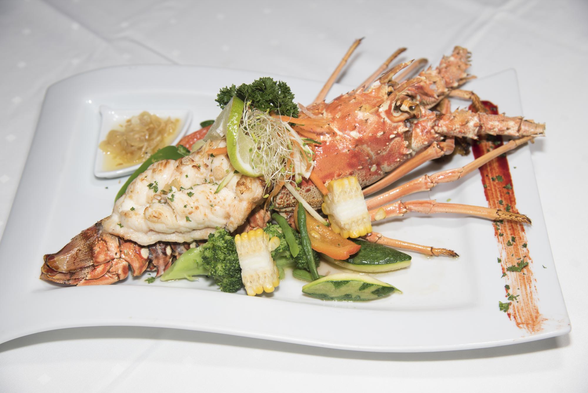 Langosta a la parrilla. Cocinada a la parrilla y acompañada por vegetales salteados en mantequilla de ajo.